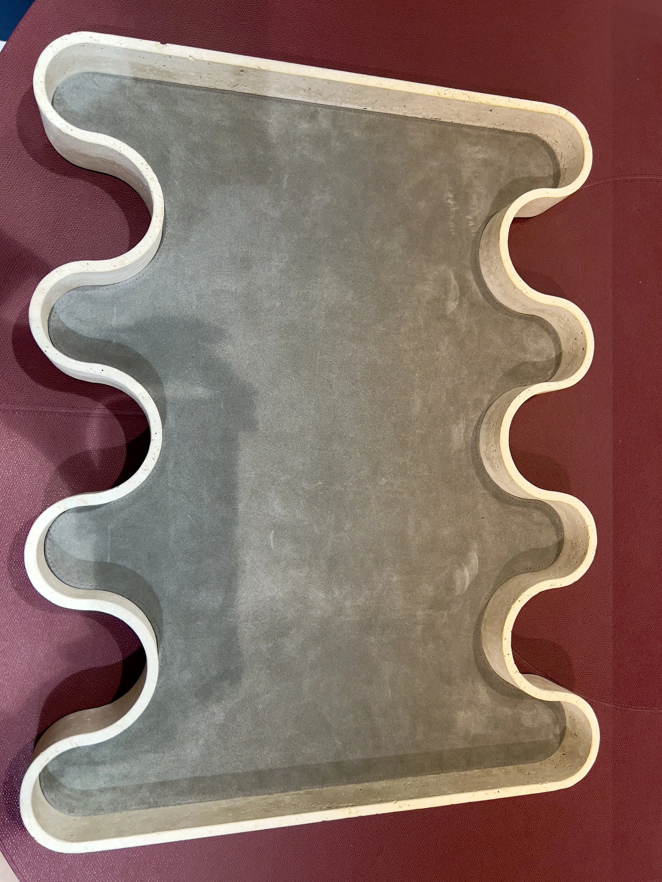 A gray tray with a wavy, irregular shape and raised edges, placed on a red surface.