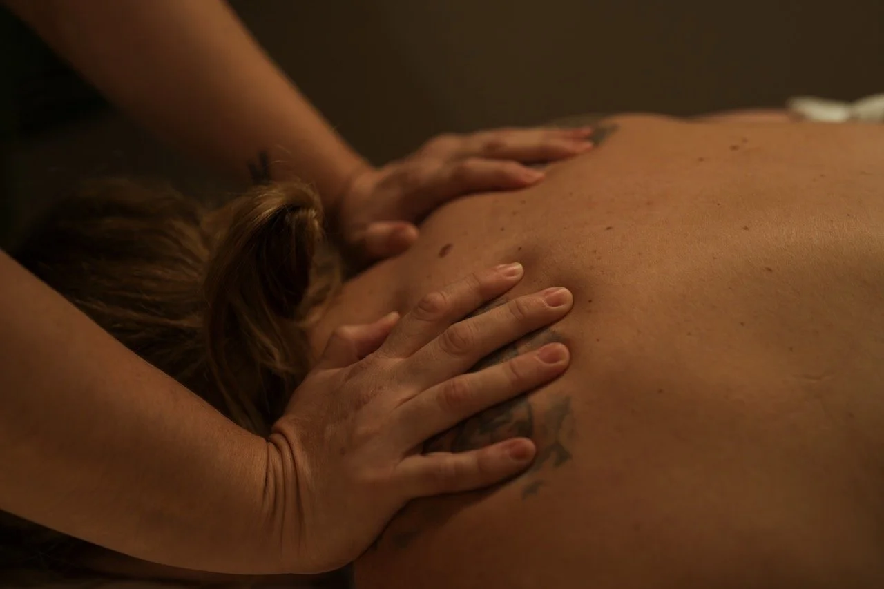 Person receiving a back massage from a massage therapist in a dimly lit room.