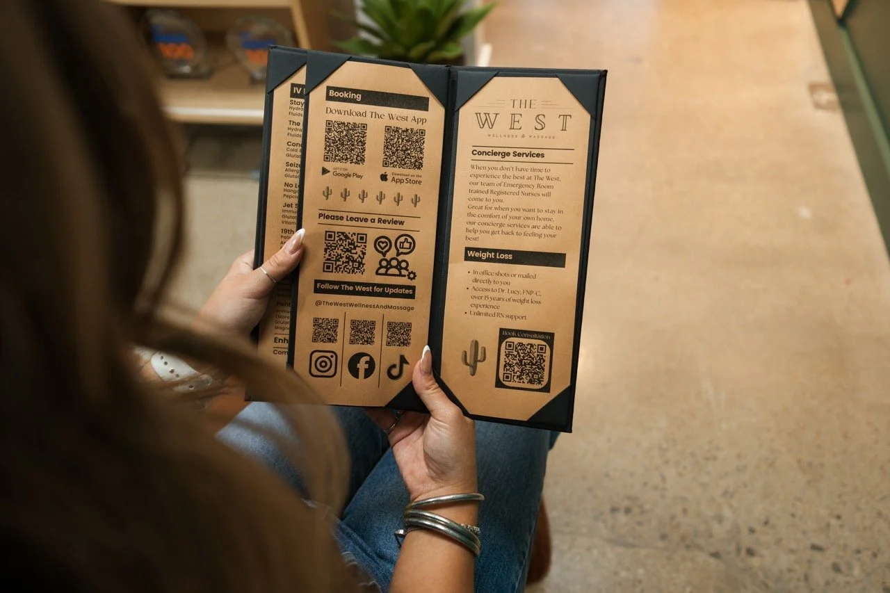 Person holding a brochure or menu with QR codes and information about wellness services at The West Wellness & Massage, including concierge services and weight loss programs.