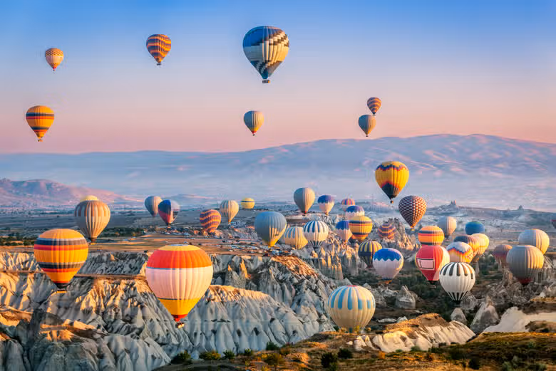Varios globos aerostáticos flotando sobre un paisaje montañoso al amanecer.