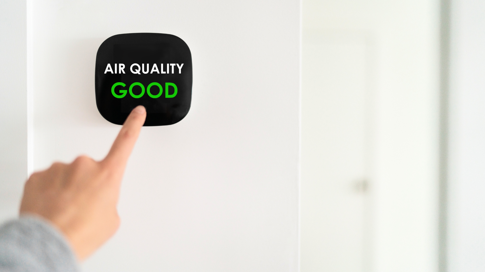 Person pressing a button on a wall that displays 'AIR QUALITY GOOD' in white and green text.