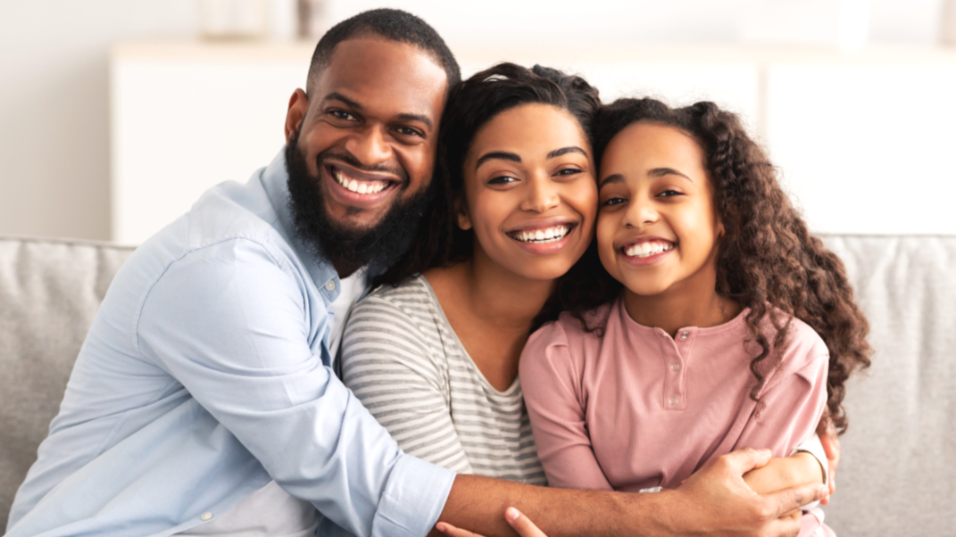 Happy family of three sitting on a couch, smiling and embracing each other