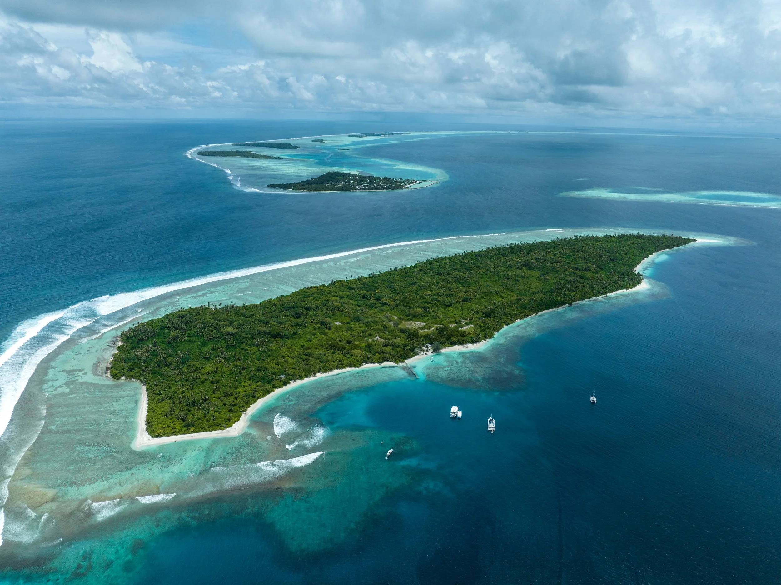 熱帯の島と周囲の青い海、白い砂浜と亀裂の入った珊瑚礁、ボートが浮かぶ