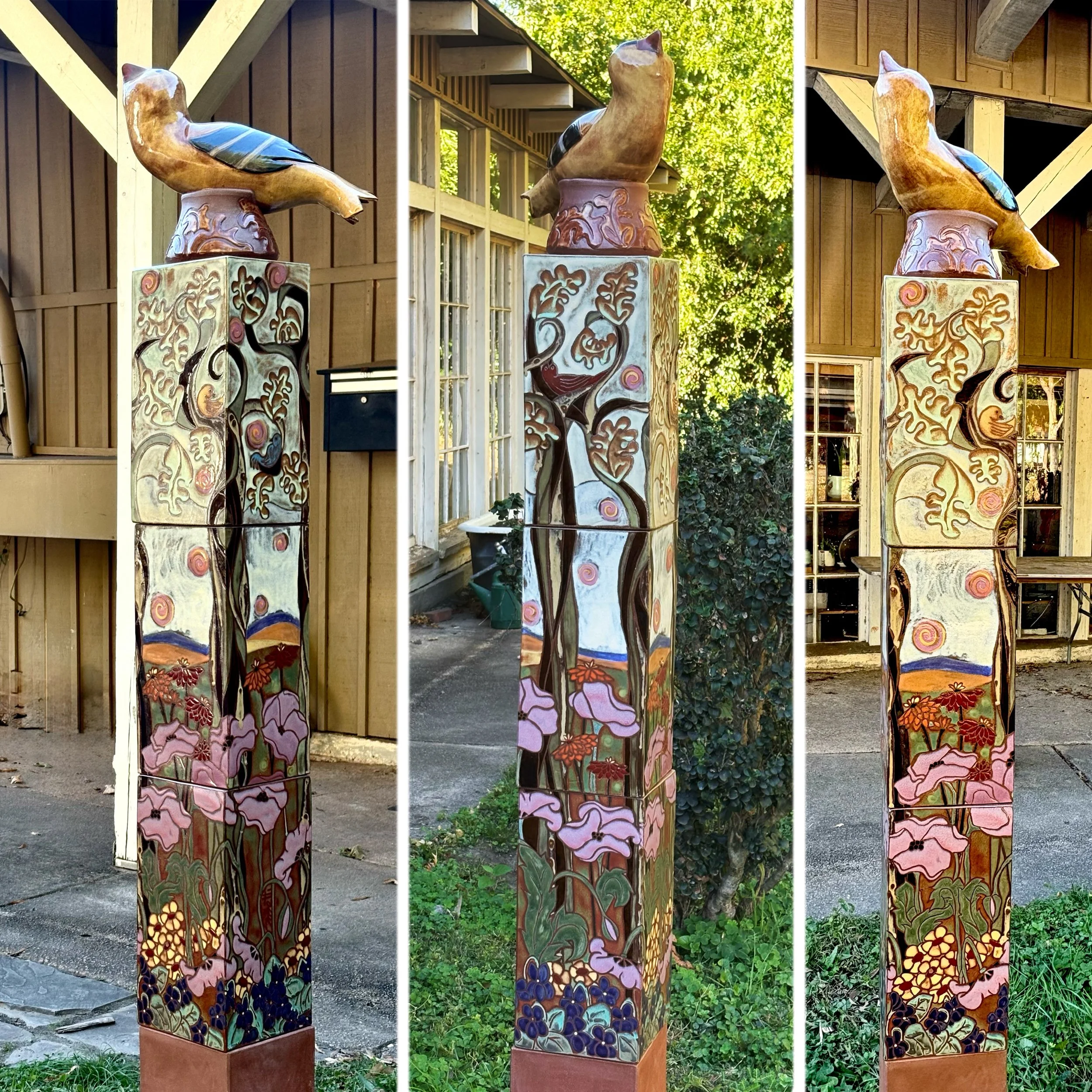 A ceramic tower of 18" x 8" x 8" decorated with trees, flowers, spirals, birds, toped with a clay sculpture of a finch.