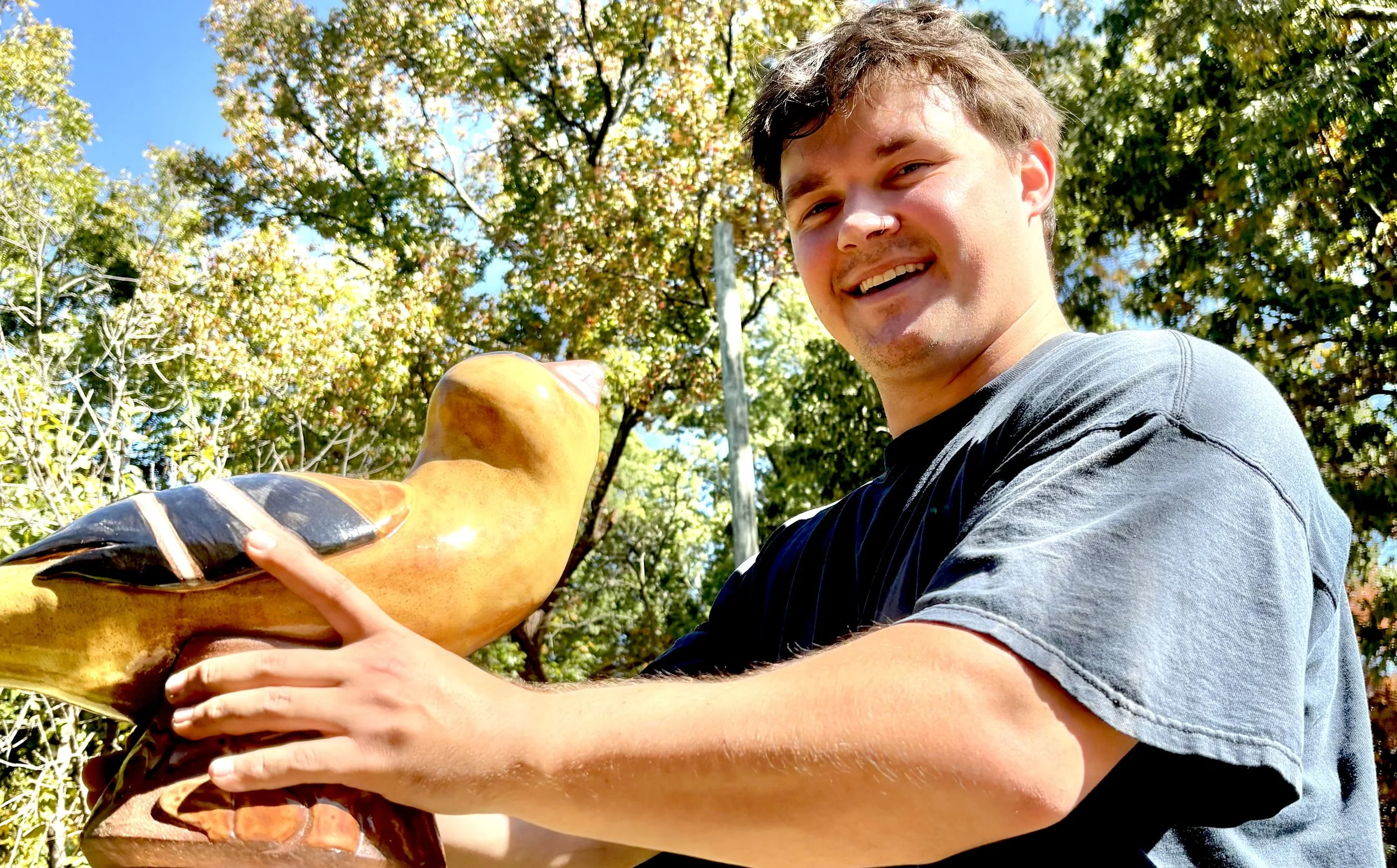 a young man with a big smile and smiling eyes hold a clay bird.