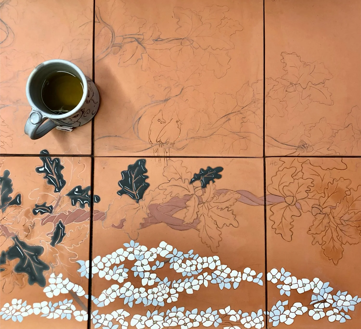 Commission in process with a mug of coffee sitting on the tiles and wet glaze drying in some leaves.