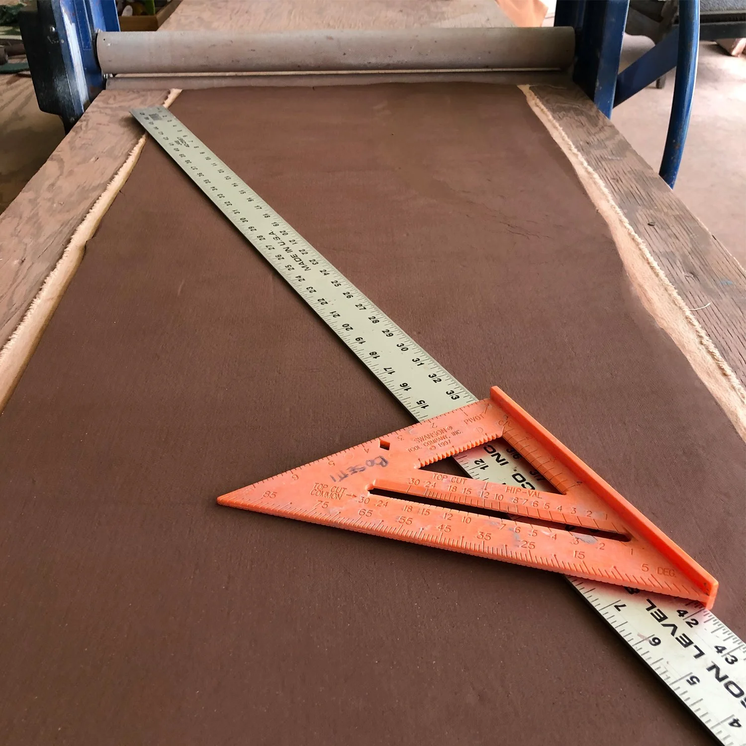 A slab of clay on a slab roller with a right angle and a four foot  metal ruler.