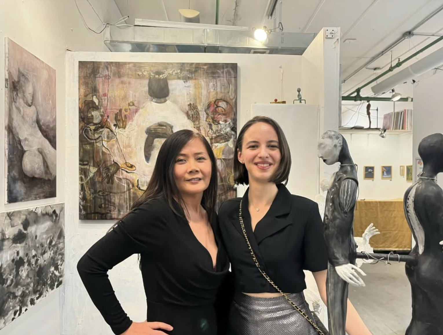 Two women standing in an art gallery, with abstract paintings and sculptures in the background.