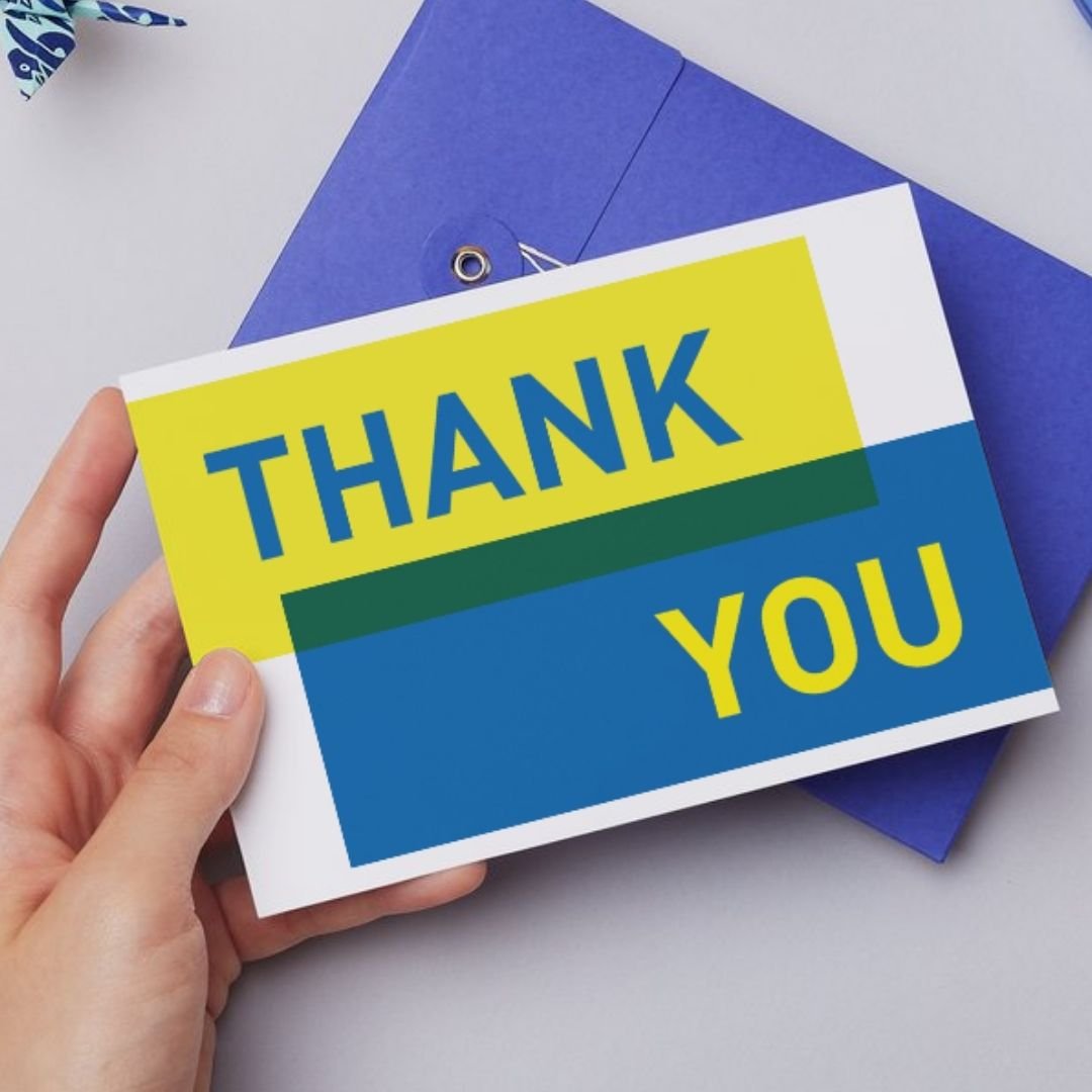 Colorful thank you card with bold letters reading 'THANK YOU' being held in front of blue envelopes and a white background.