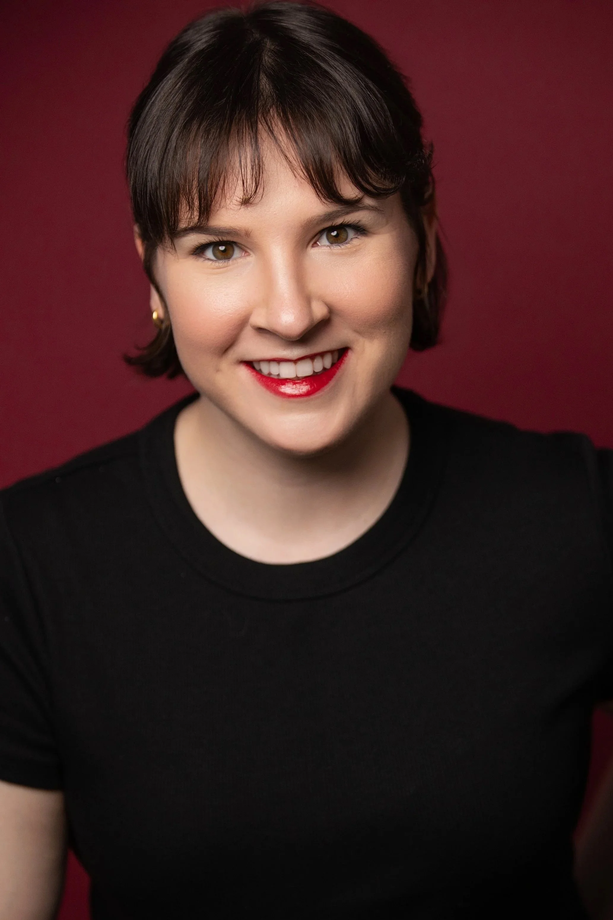 Katie Jacoby's portrait smiling in a black shirt on a burgundy backdrop.