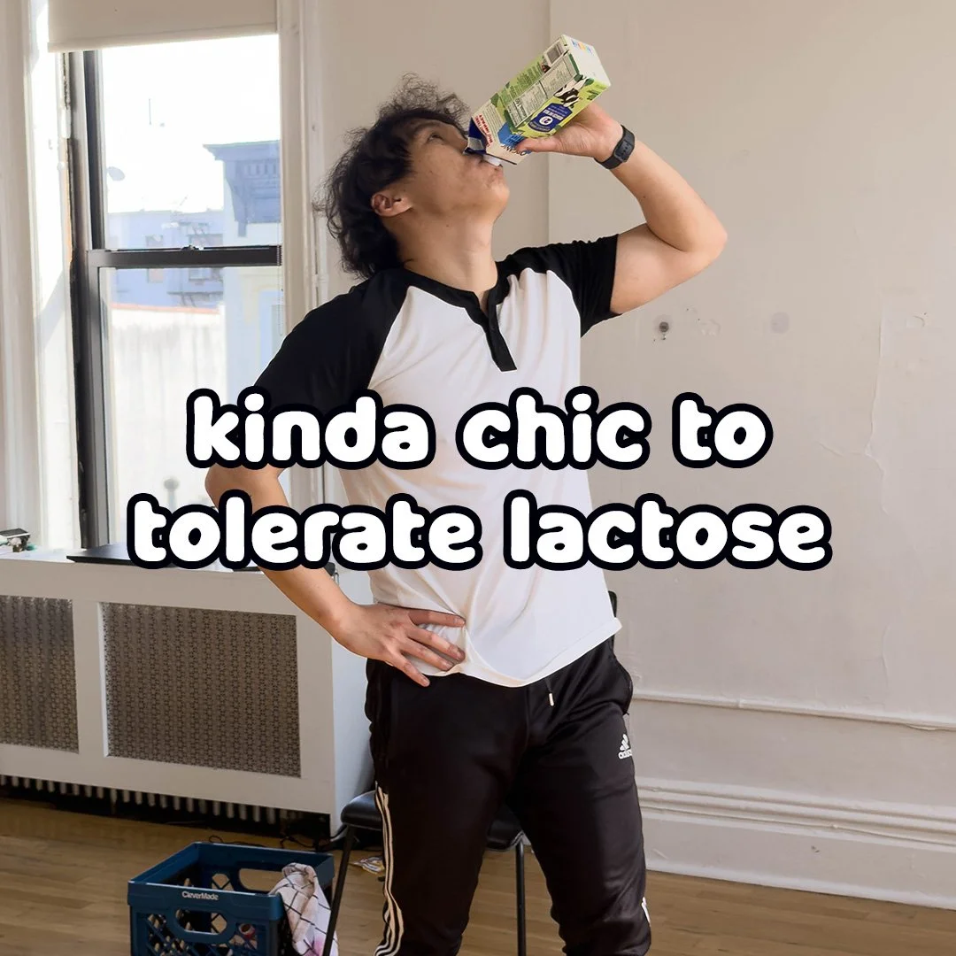A person with curly hair drinking from a box of lactase alternative milk in a room with large windows, wearing a black and white t-shirt and black Adidas pants, with a caption that reads, 'kinda chic to tolerate lactose'.