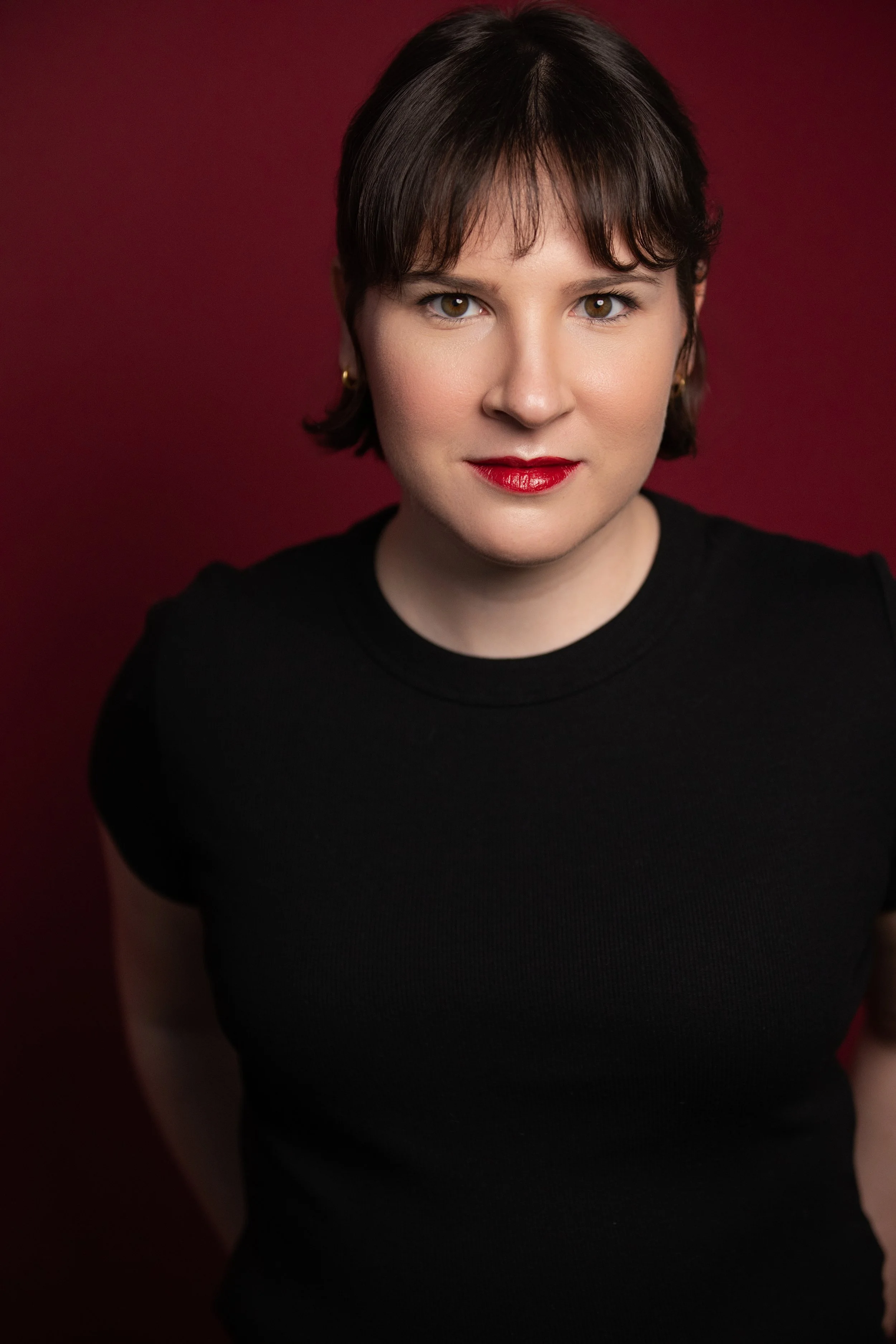 Katie Jacoby's portrait with a slightly serious expression on a burgundy background.