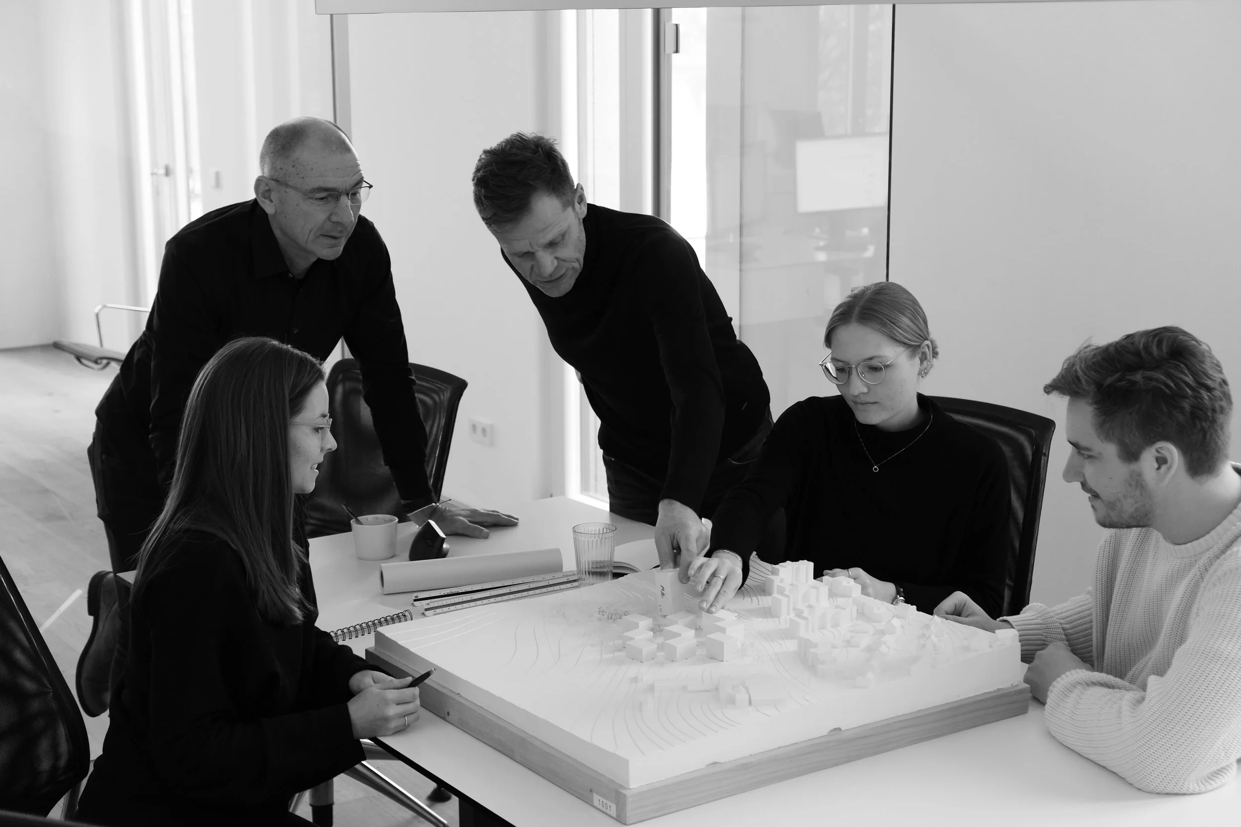 Fünf Menschen diskutieren um einen Modell-Architekturprojekt in einem Besprechungsraum.