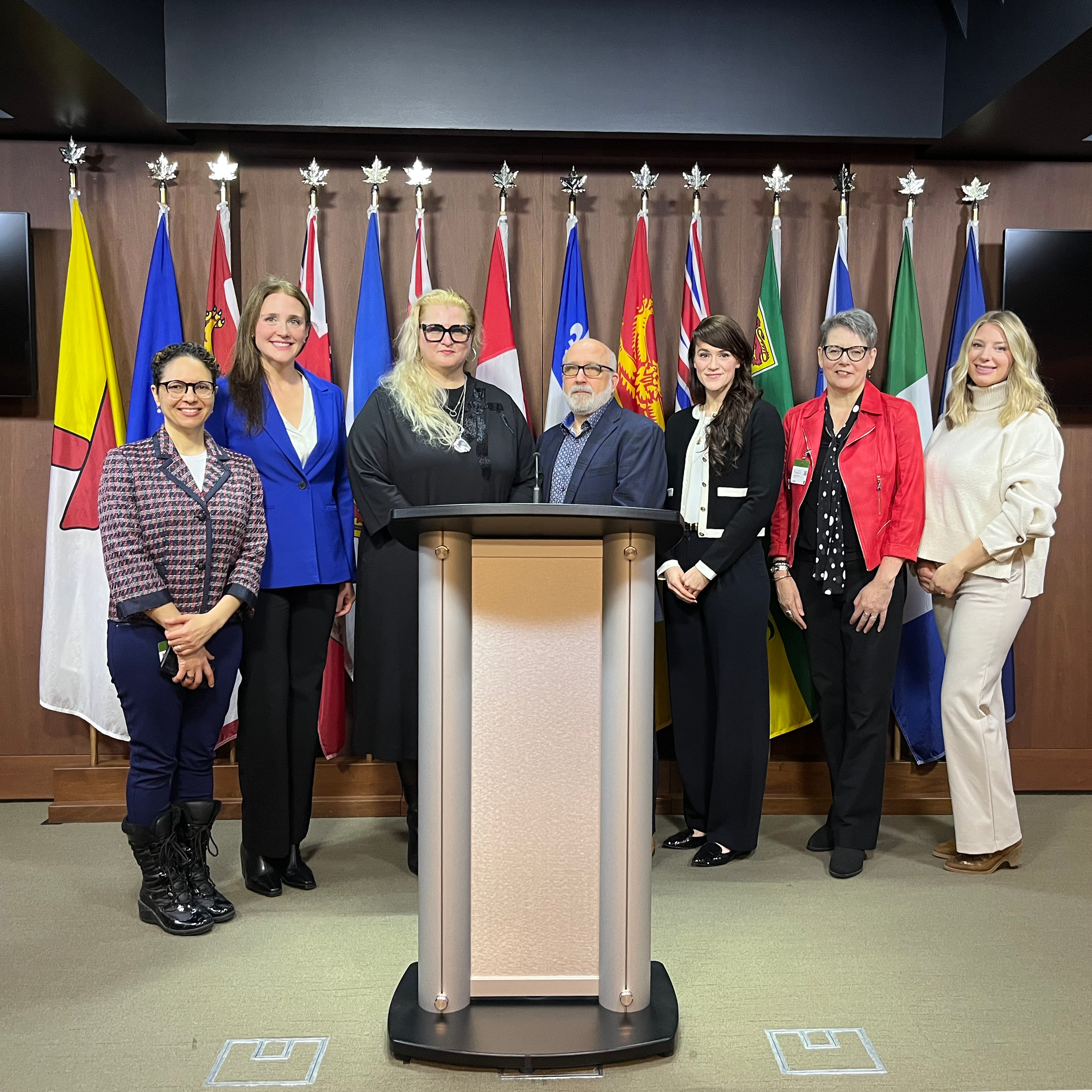 A group of diverse people standing in front of a row of flags.