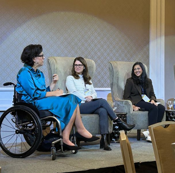 Three women engaged in conversation. One woman is in a wheelchair and speaking to the others.