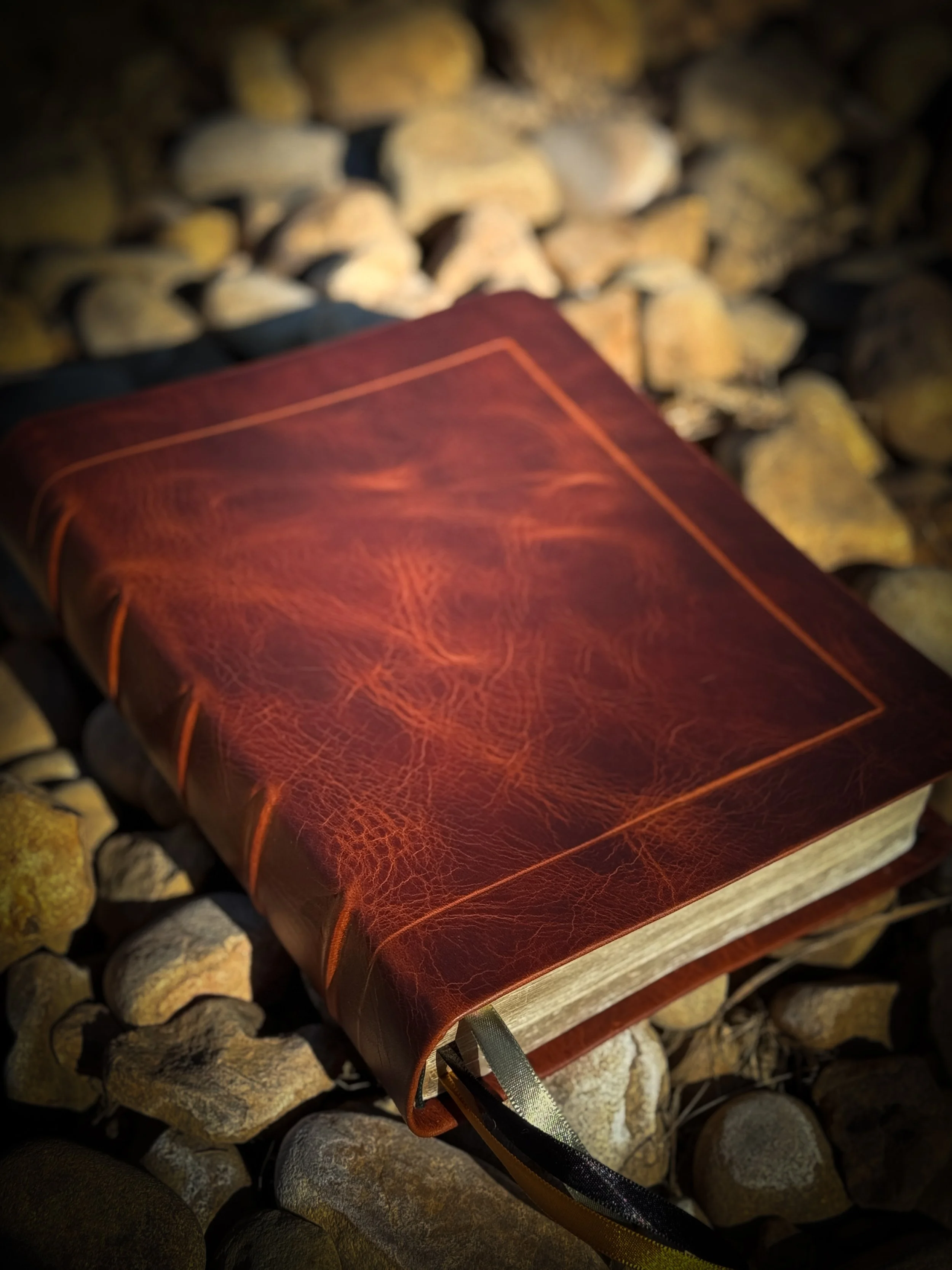 A leather-bound journal resting on a bed of rocks.