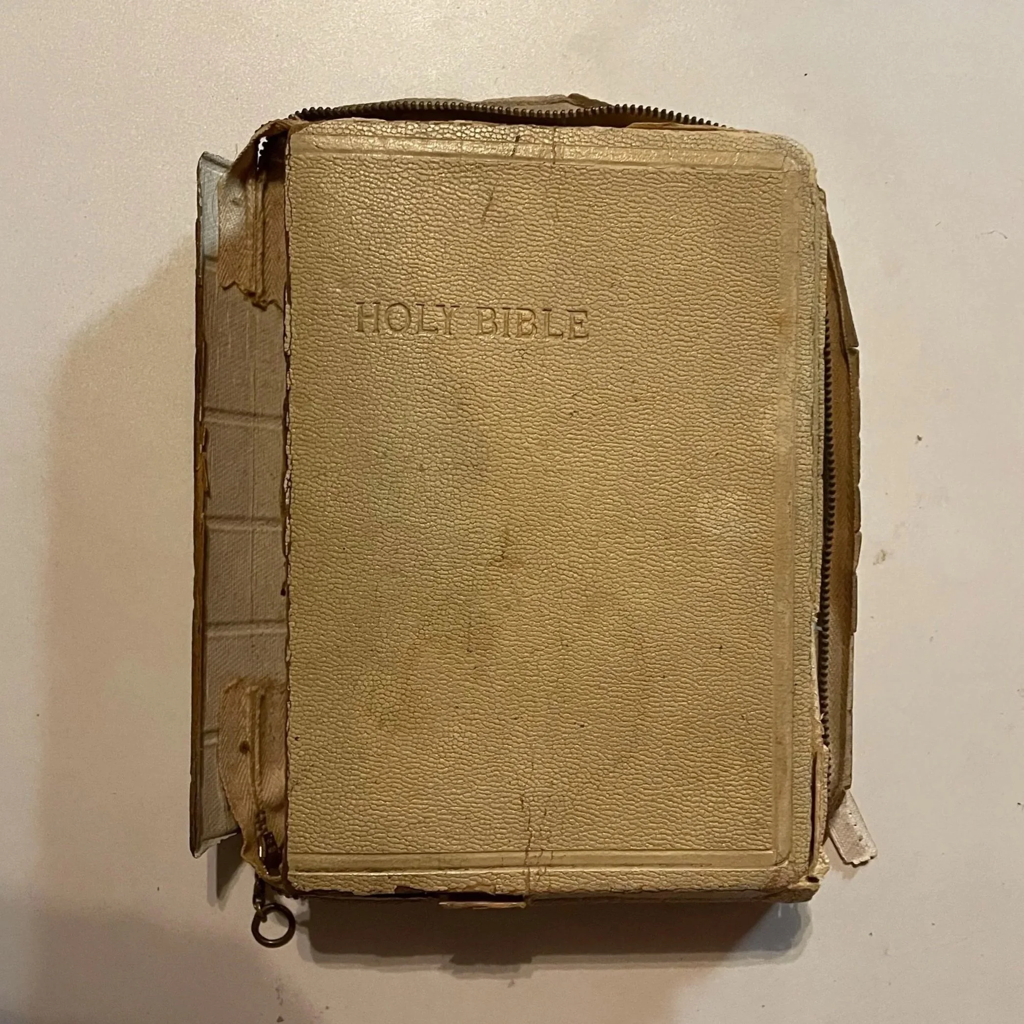 An old, worn, yellowish leather-bound Holy Bible with visible cracks and a zipper around it.