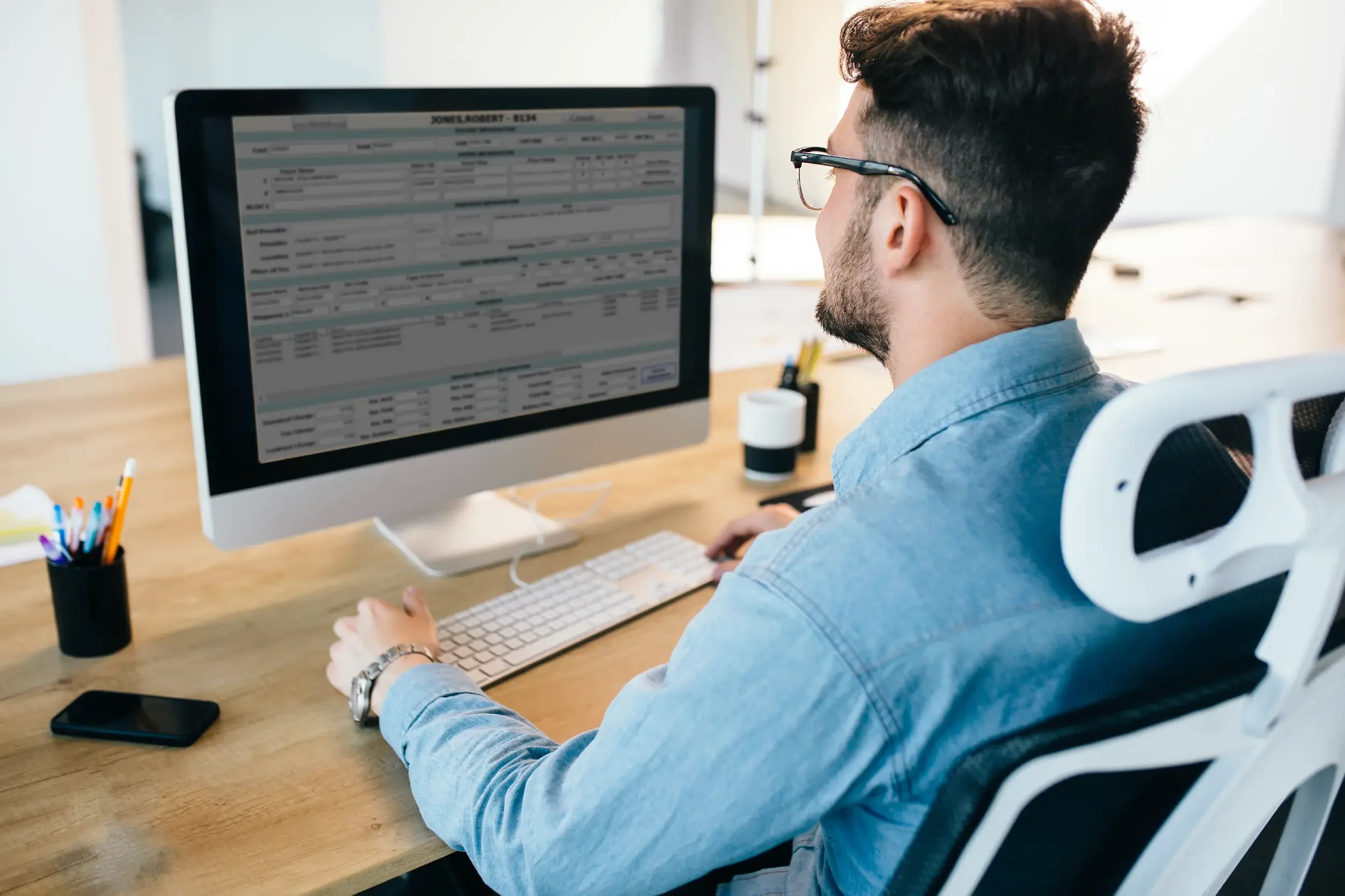 Man working on a desktop computer displaying a spreadsheet in a modern office.