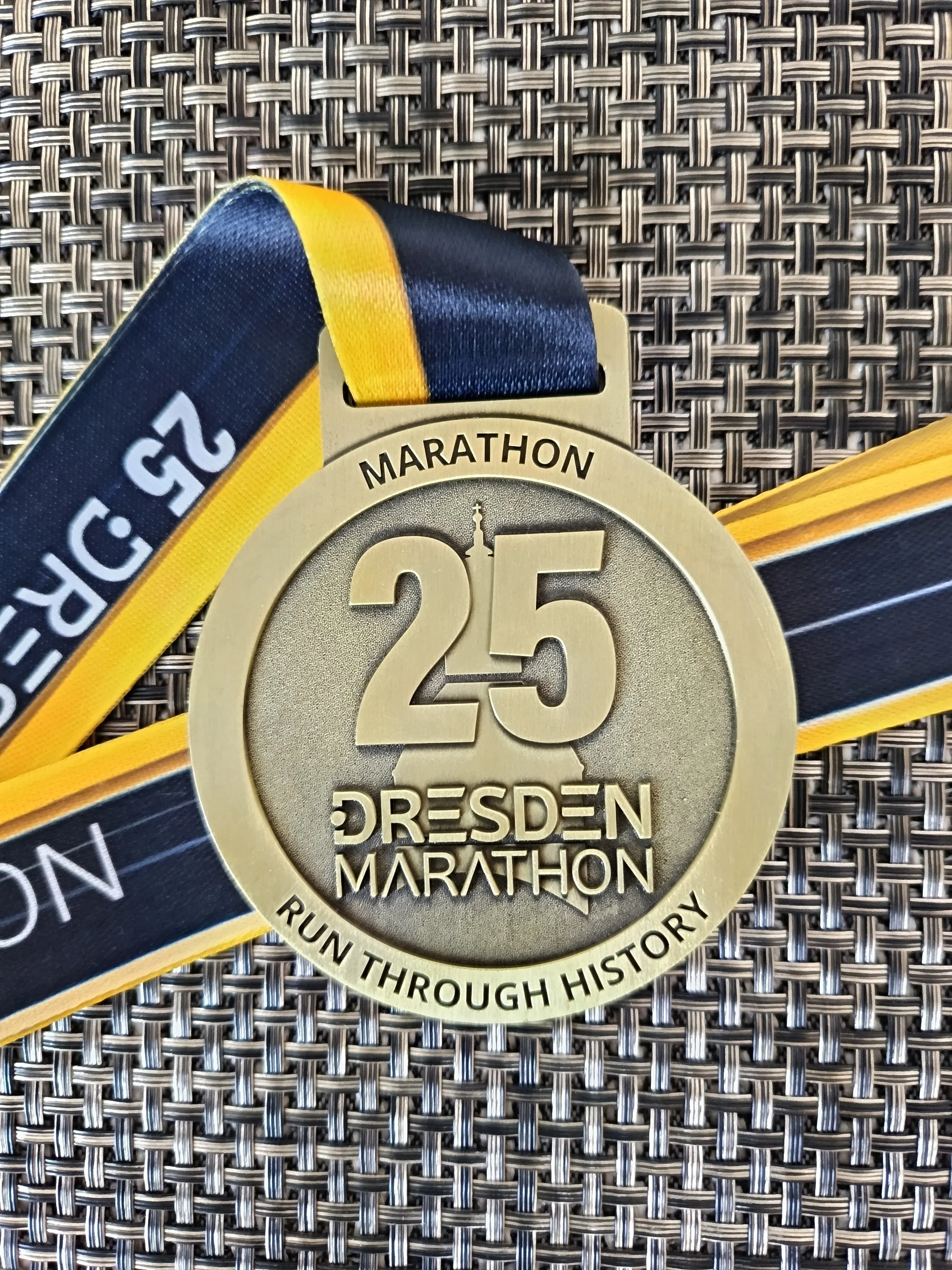 Goldene Medaille für den Dresden Marathon, 25. Marathon, mit schwarzem, gelbem Band, auf Holzuntergrund.