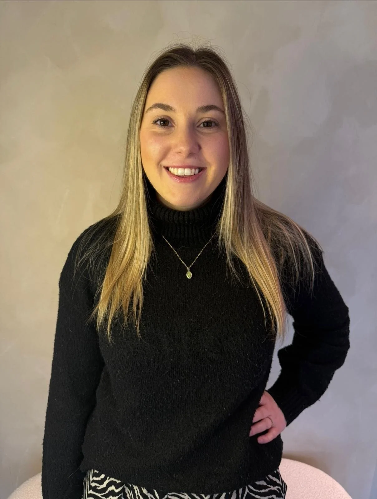 A smiling woman with curly hair, wearing glasses, hoop earrings, and a striped shirt, in a bright indoor setting.