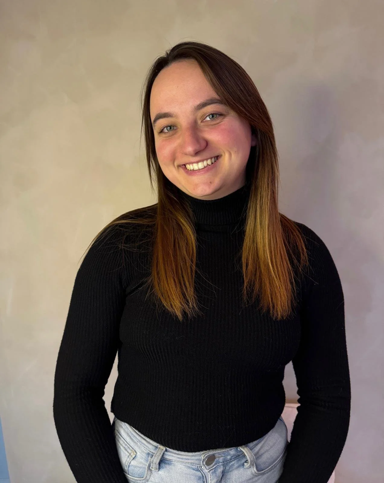 A young woman with short black hair smiling in a green, leafy environment.