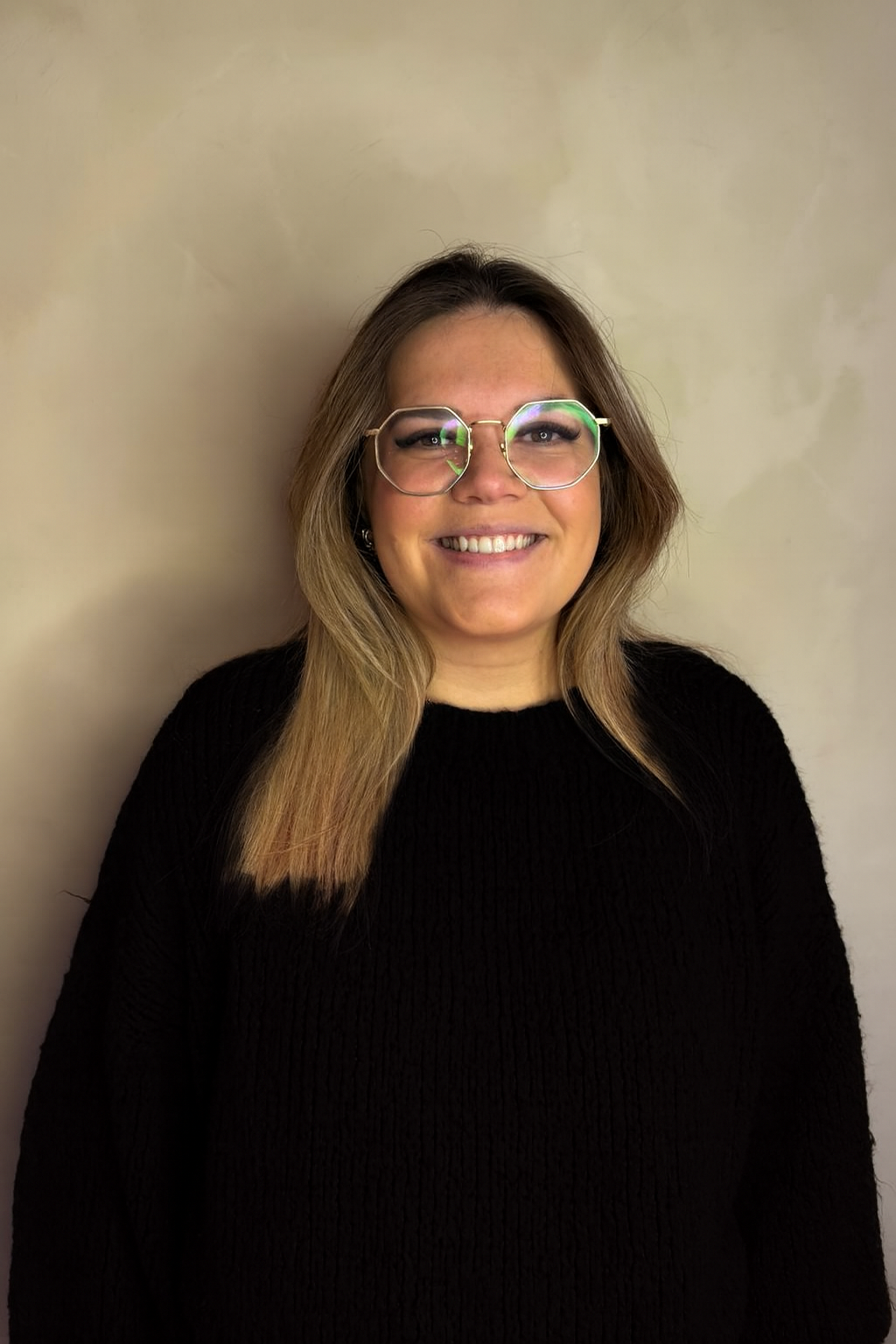 A young Asian woman with shoulder-length black hair, smiling and showing her teeth, in front of green plants and leaves.