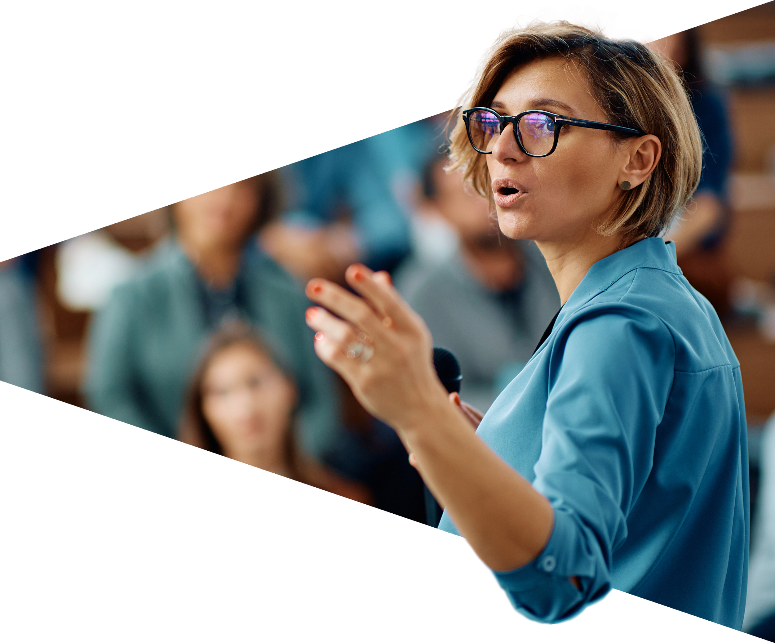 A woman with short blonde hair, glasses, and a blue blazer speaking in front of an audience in a classroom or seminar setting.