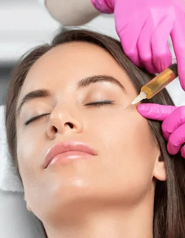 A woman receiving a cosmetic injection in her cheek from a healthcare professional wearing pink gloves.
