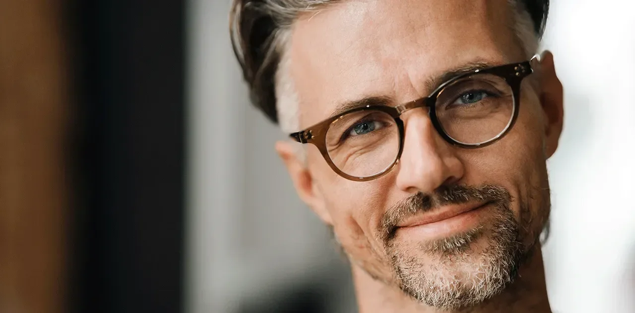 Close-up of a middle-aged man with dark hair, glasses, and a beard, smiling softly.
