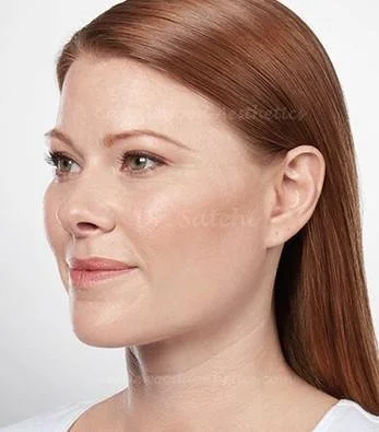Close-up of a woman with straight red hair and fair skin, looking slightly to her left with a neutral expression.