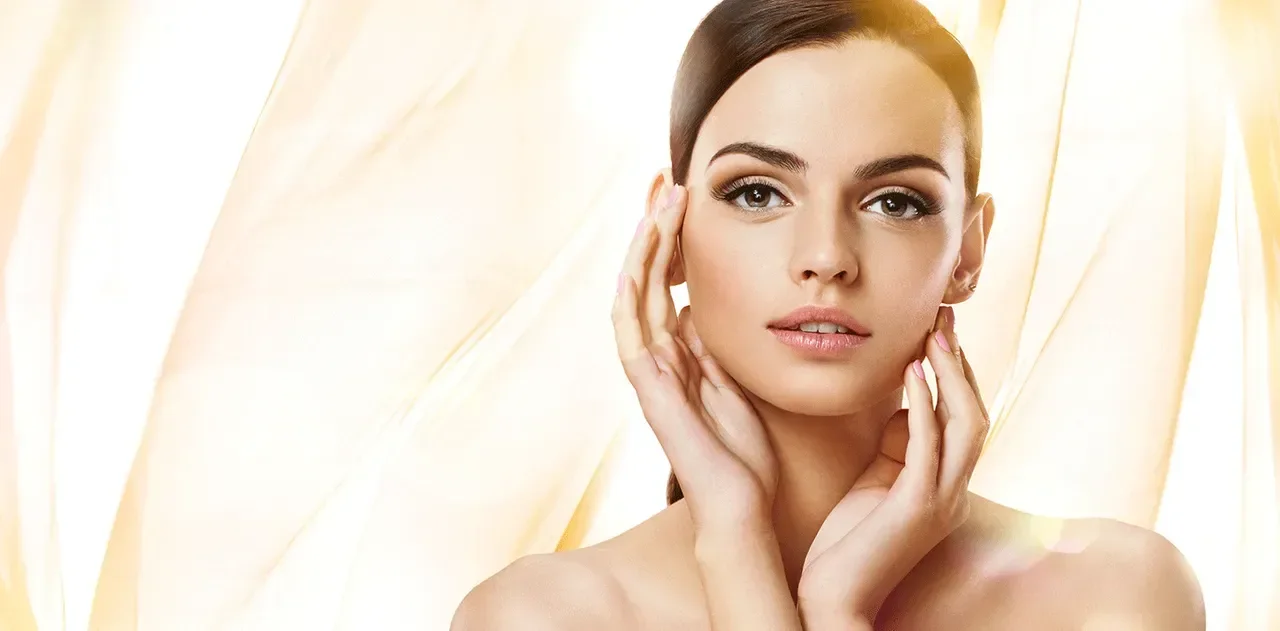 A woman with smooth skin and dark hair posing against a soft, warm background.