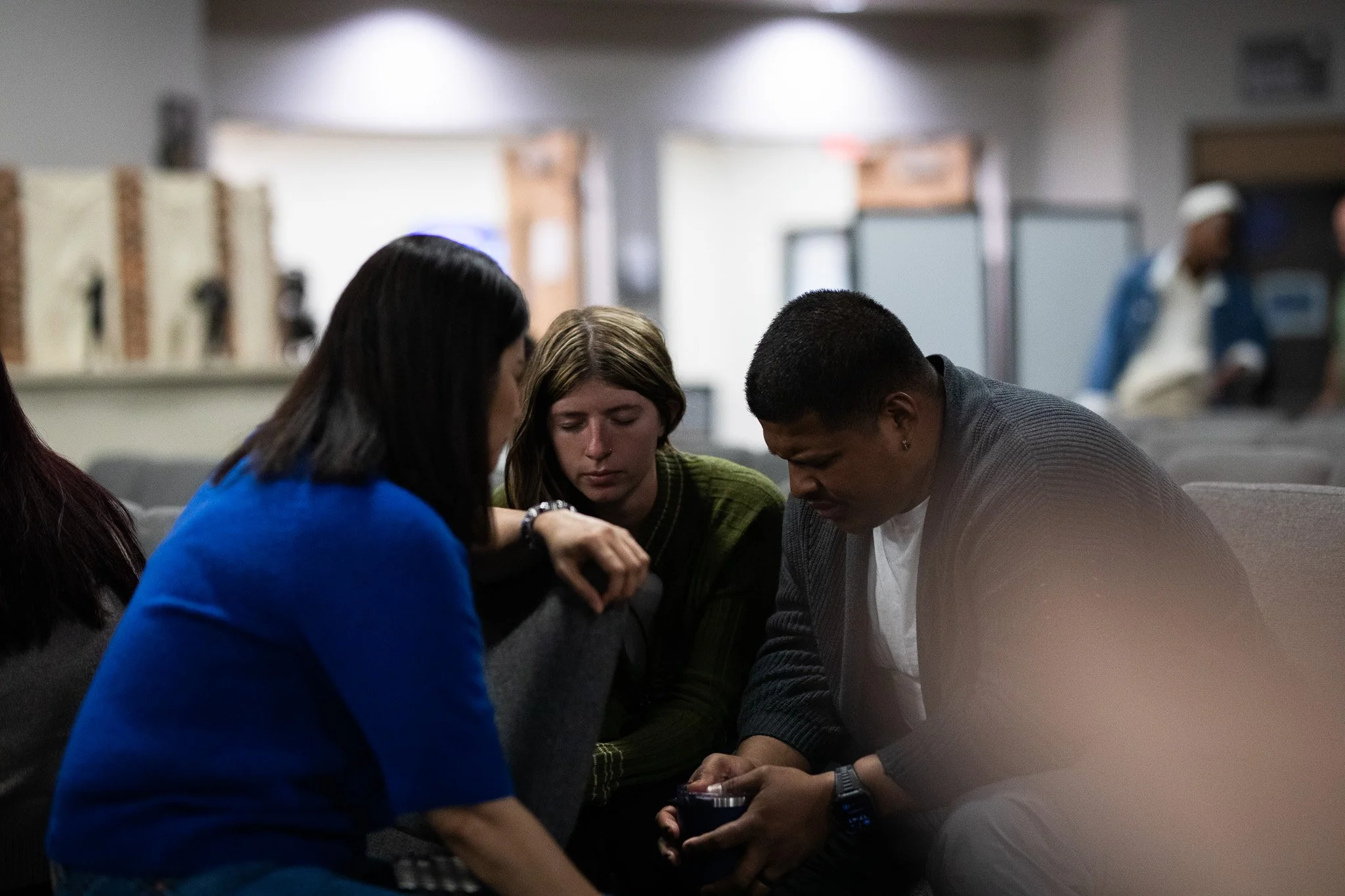Four people sitting closely together, looking down at something in their hands, in a room with blurred background.