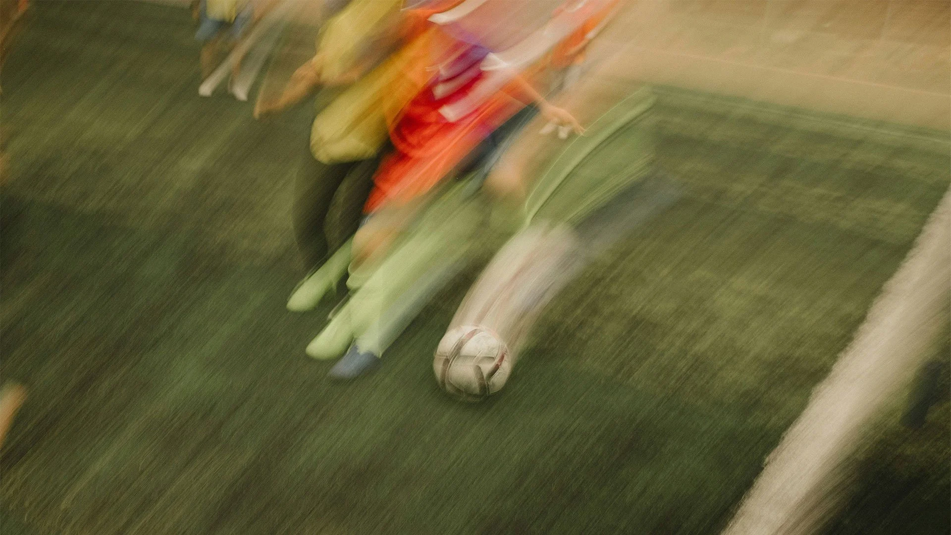 Blurred image of a person lying on a hospital bed with a foot cast, next to a soccer ball on the floor.