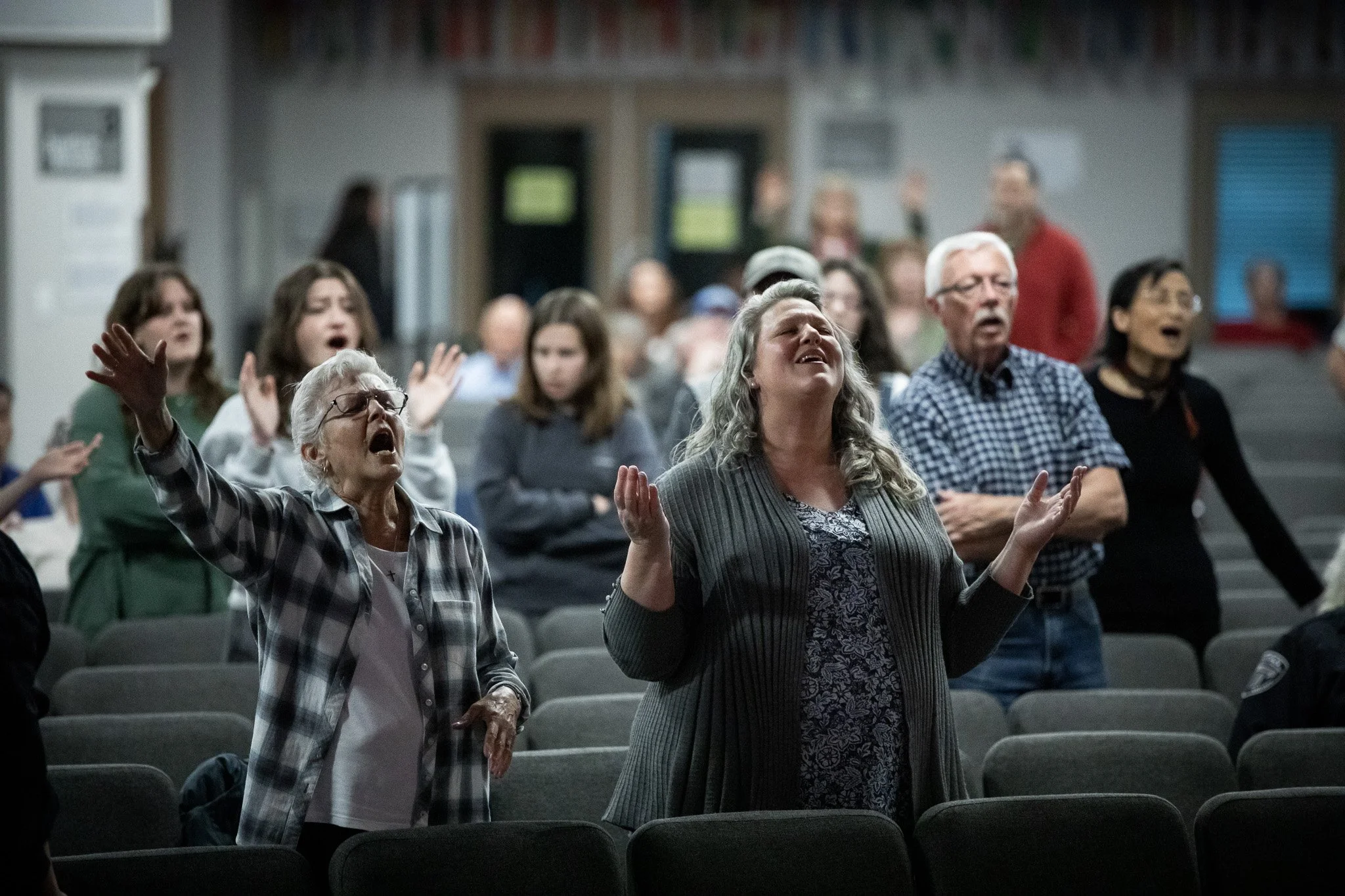 A diverse group of people, including elderly women and men, praying with their eyes closed and hands raised in a church or worship setting.