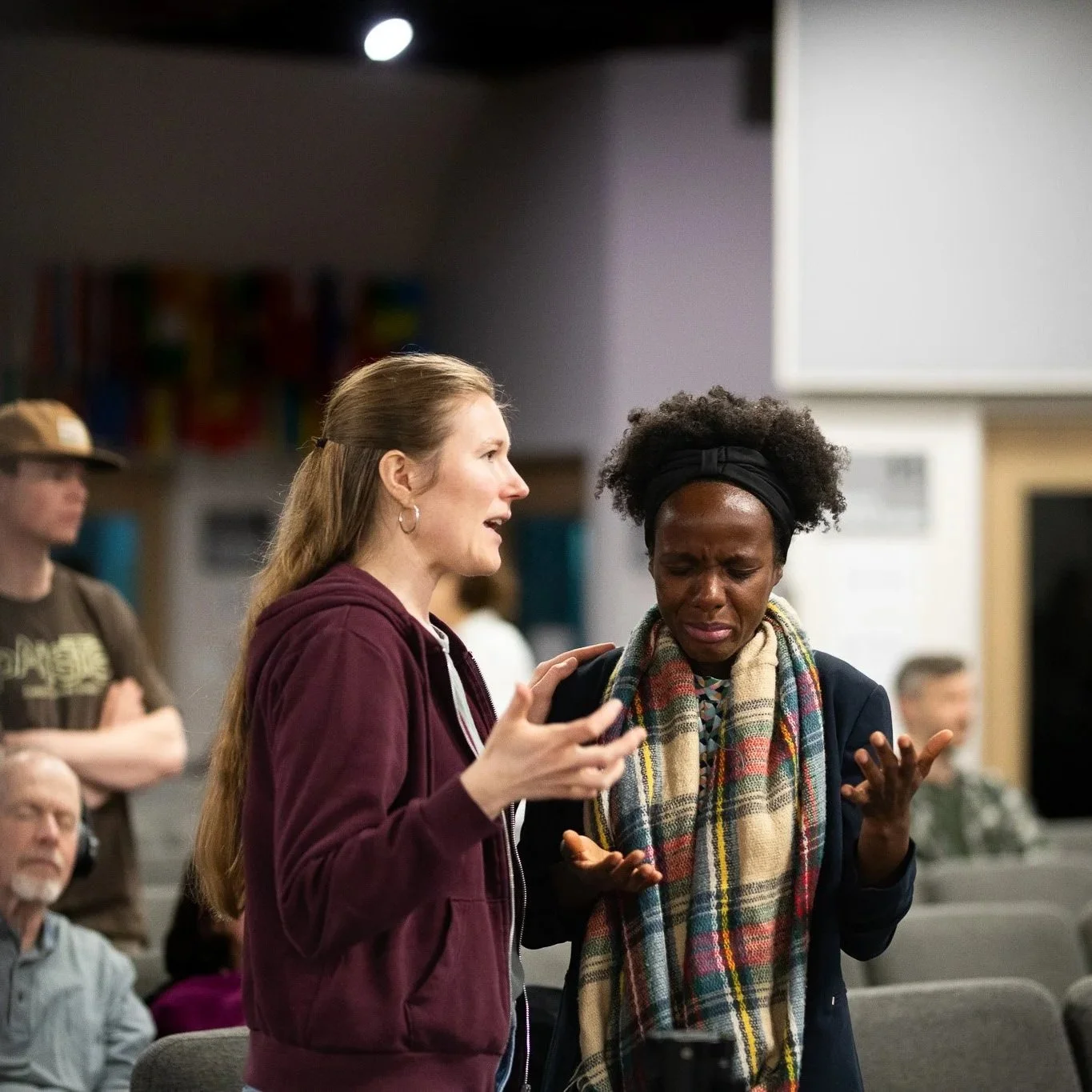 Two women are in a conversation in a public indoor setting. One woman is speaking passionately while the other appears upset and is crying.