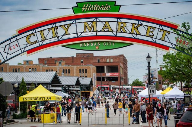 Crowd entering Kansas City's historic City Market with a large colorful sign overhead and yellow information tent.