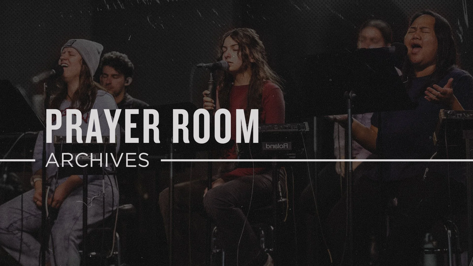A group of people singing and playing musical instruments in a prayer room or worship setting, with the words "PRAYER ROOM ARCHIVES" overlayed on the image.