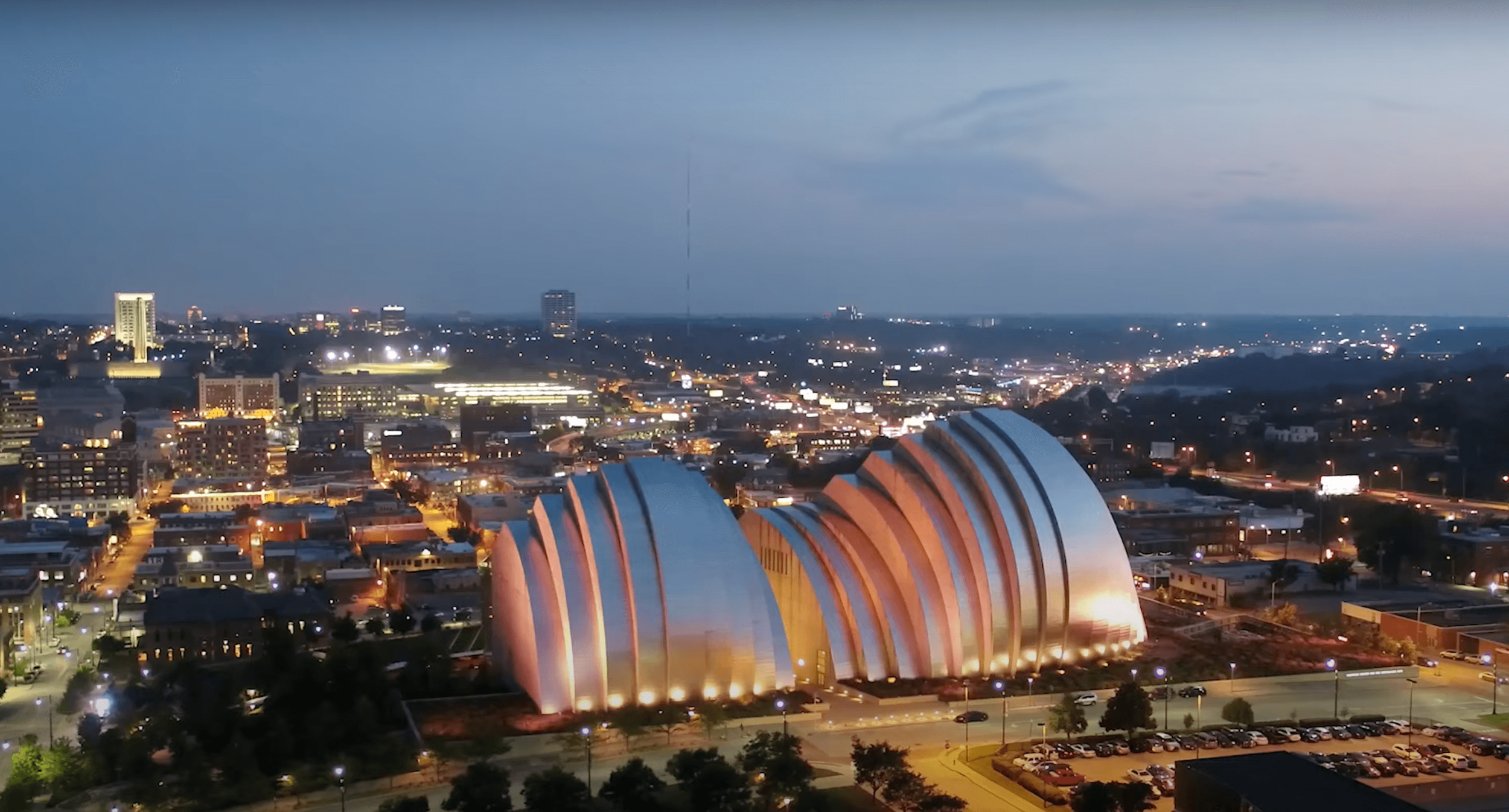 Night cityscape featuring illuminated buildings and streets, with a distinctive modern, curved architectural structure in the foreground.