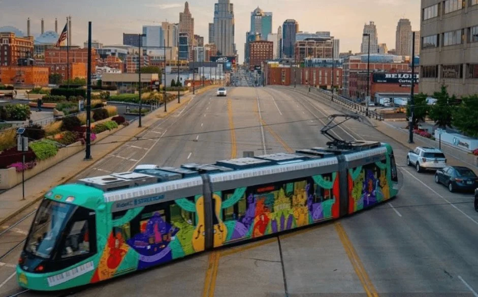 Colorful modern tram with vibrant graphic artwork on street with city skyline in background.