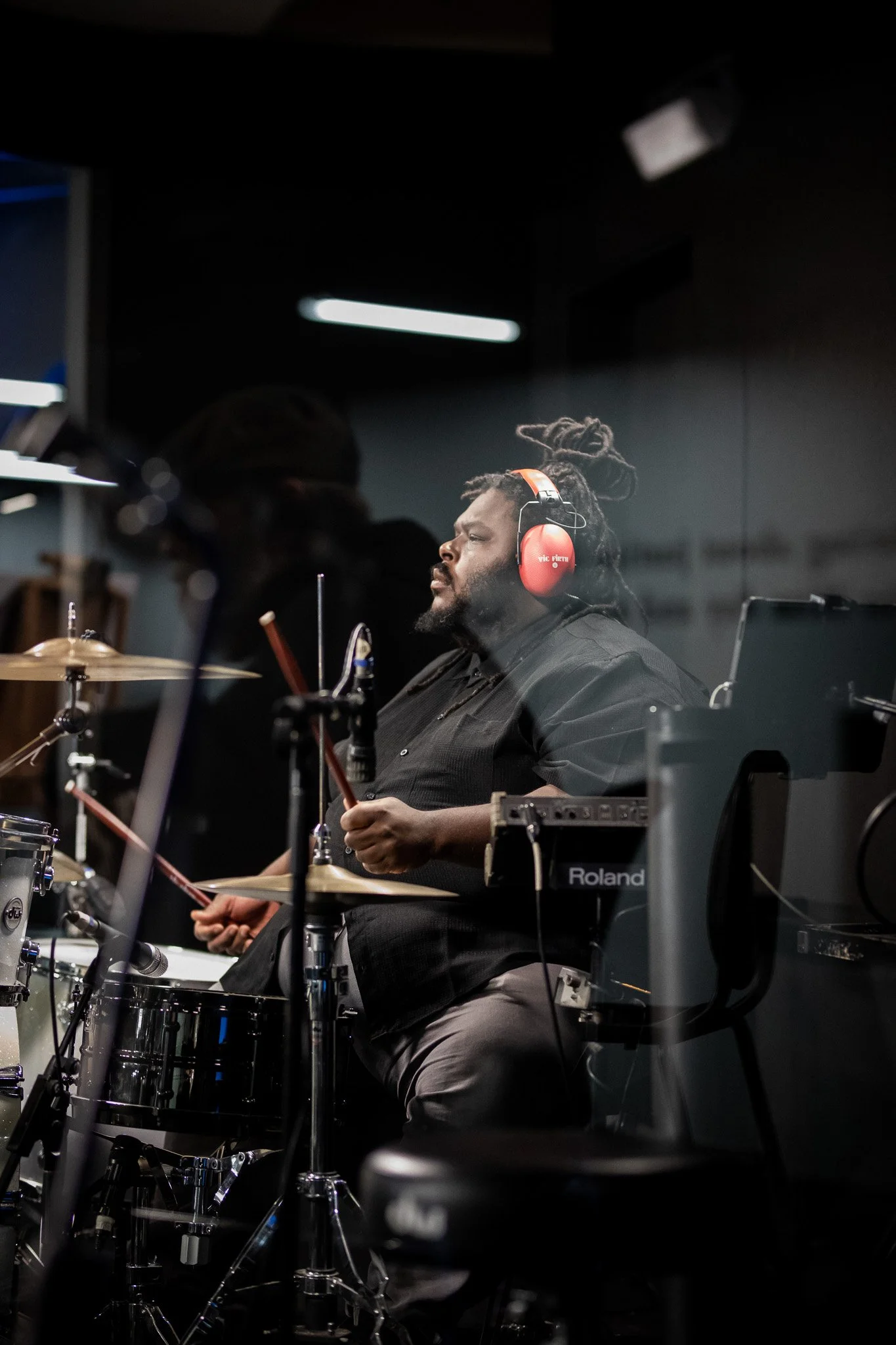 A man with dreadlocks wearing red headphones playing drums in a music studio.