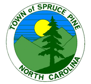 Town of Spruce Pine logo featuring a large pine tree, mountains, a yellow sun, and a blue sky surrounded by a white circular border with green text.