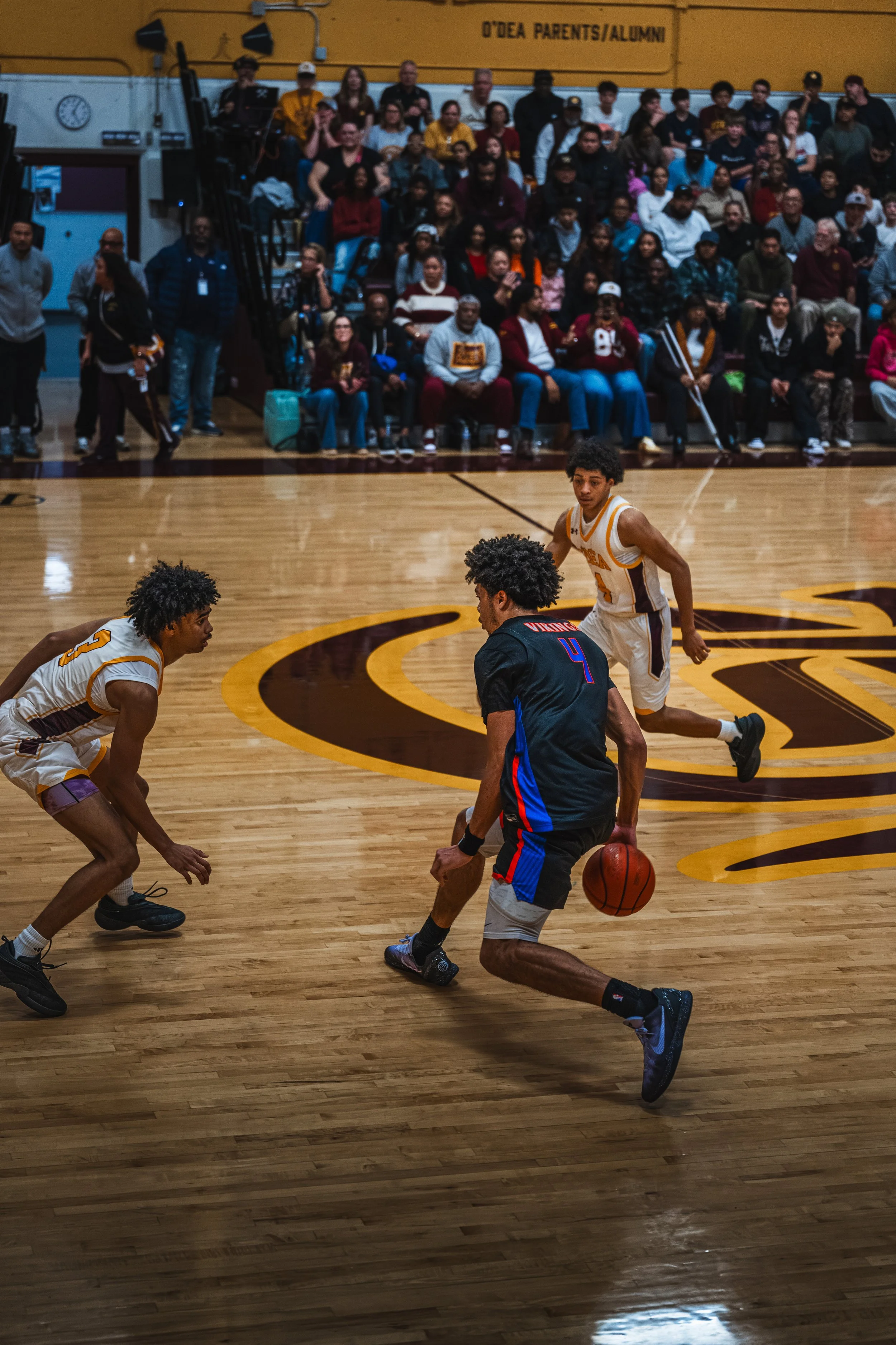 Basketball game with three players on the court and a crowd watching in the background.