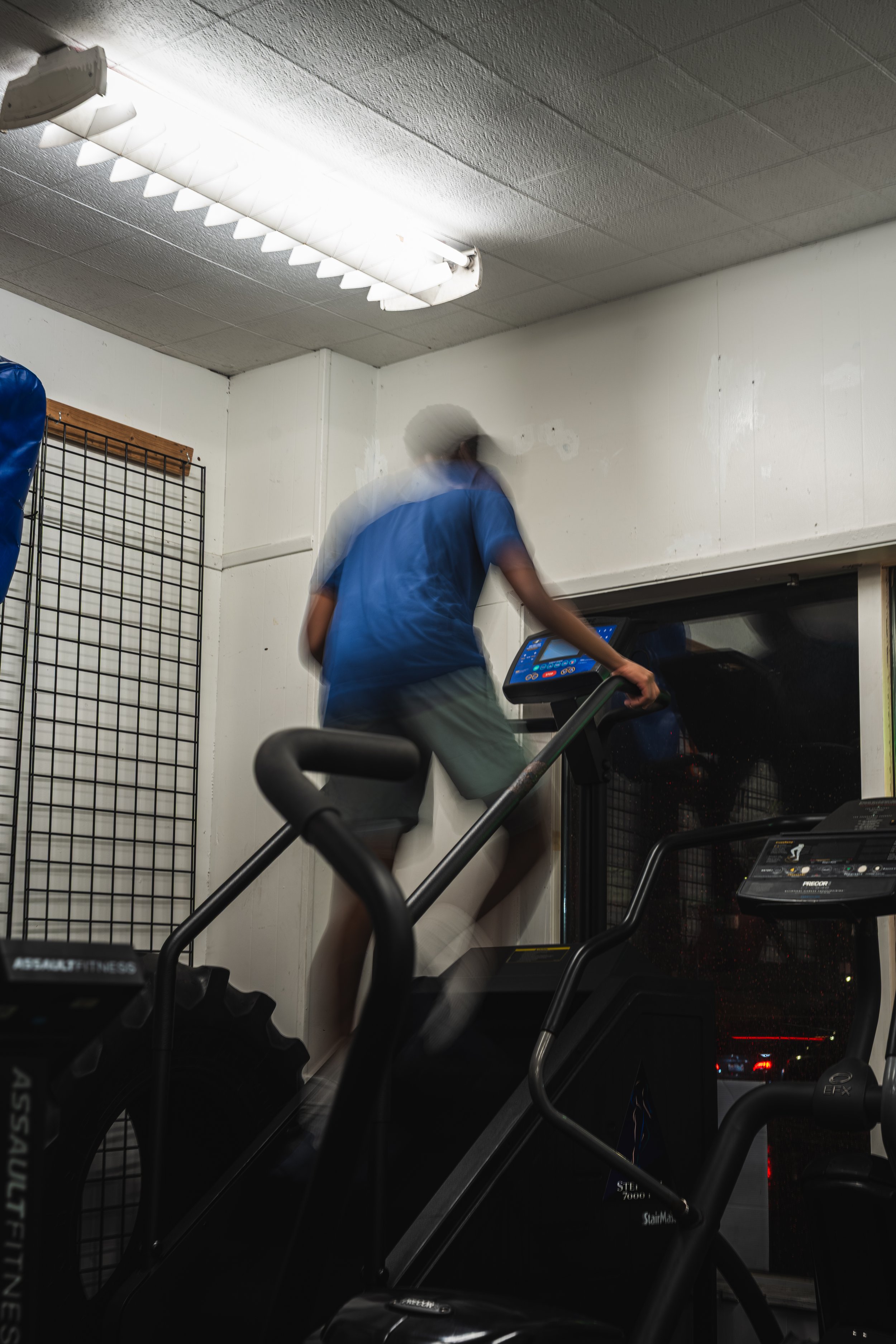 A person running on a treadmill in a gym, with motion blur indicating movement, indoor lighting, and gym equipment visible in the background.