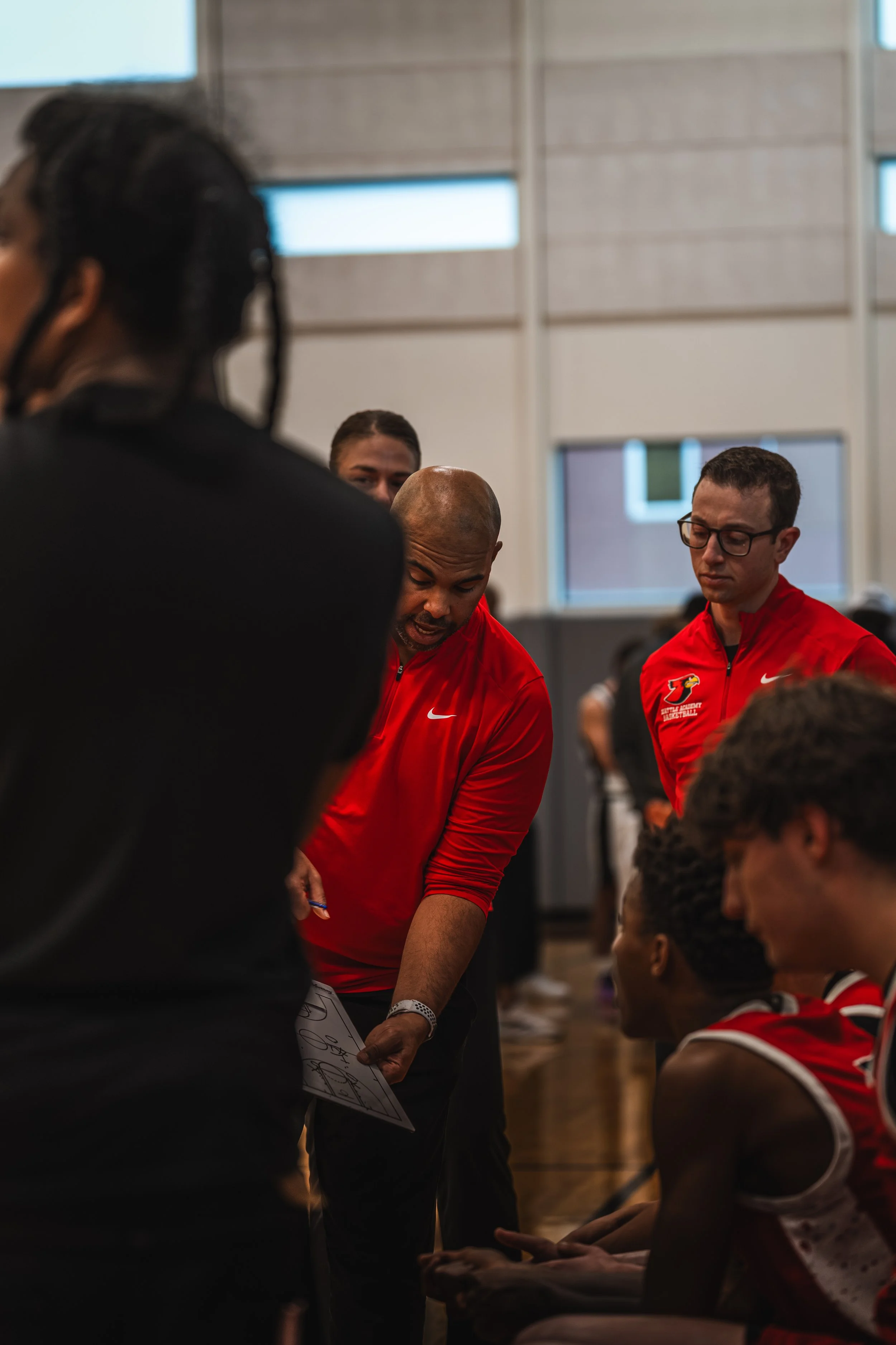 Basketball coach giving instructions to a team during a timeout in a gymnasium.