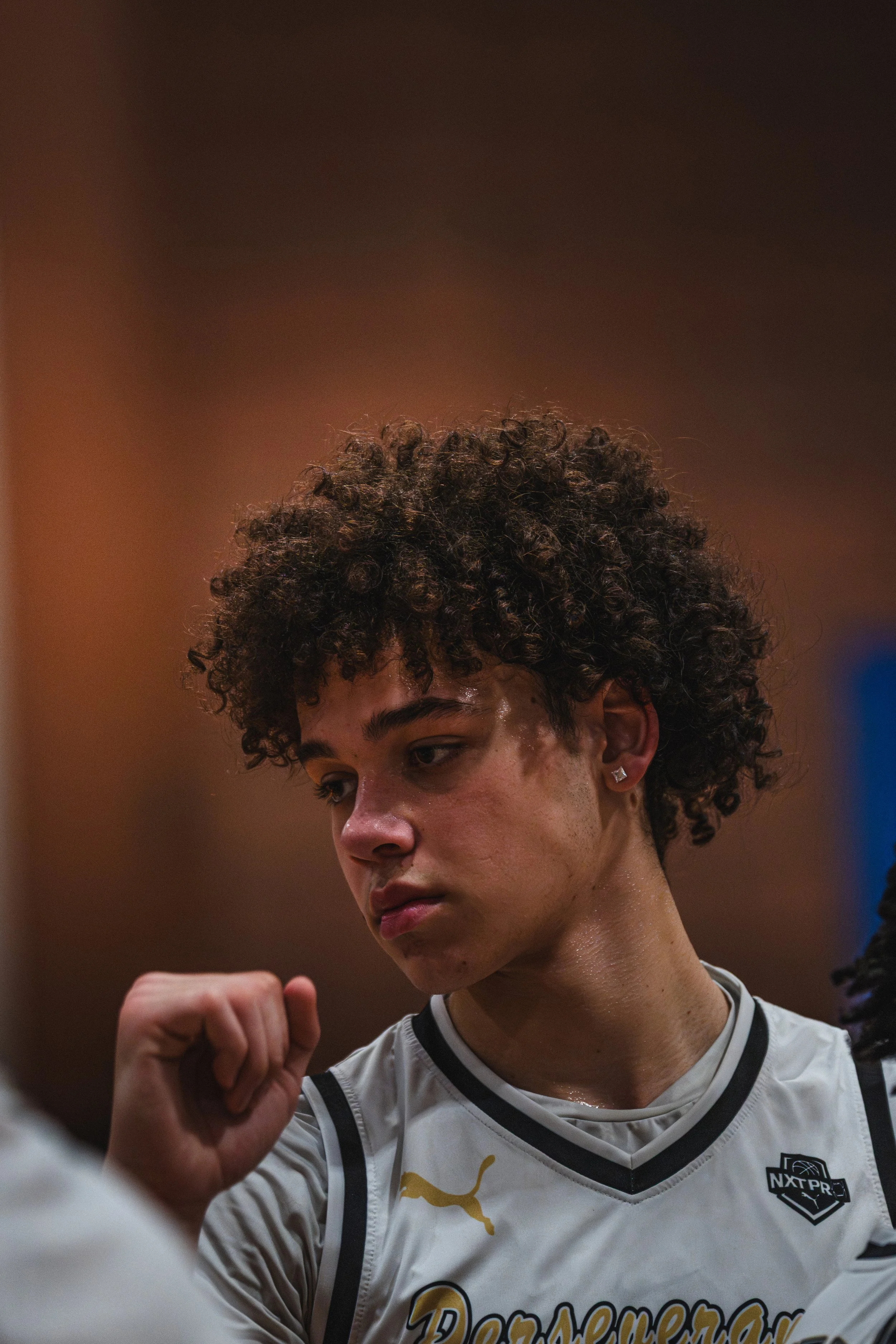 A young woman with curly hair looking down with a serious expression, wearing a sports jersey.