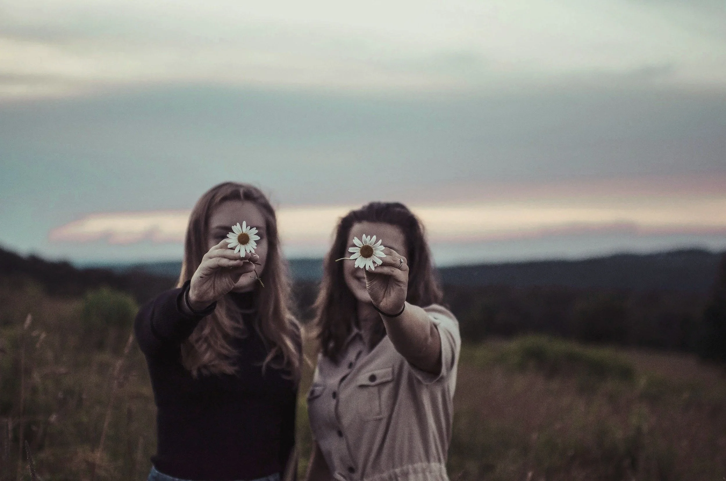 Zwei Frauen halten Daumen und Zeigefinger mit einer Gänseblümchen in den Himmel, im Freien bei Sonnenuntergang oder Dämmerung