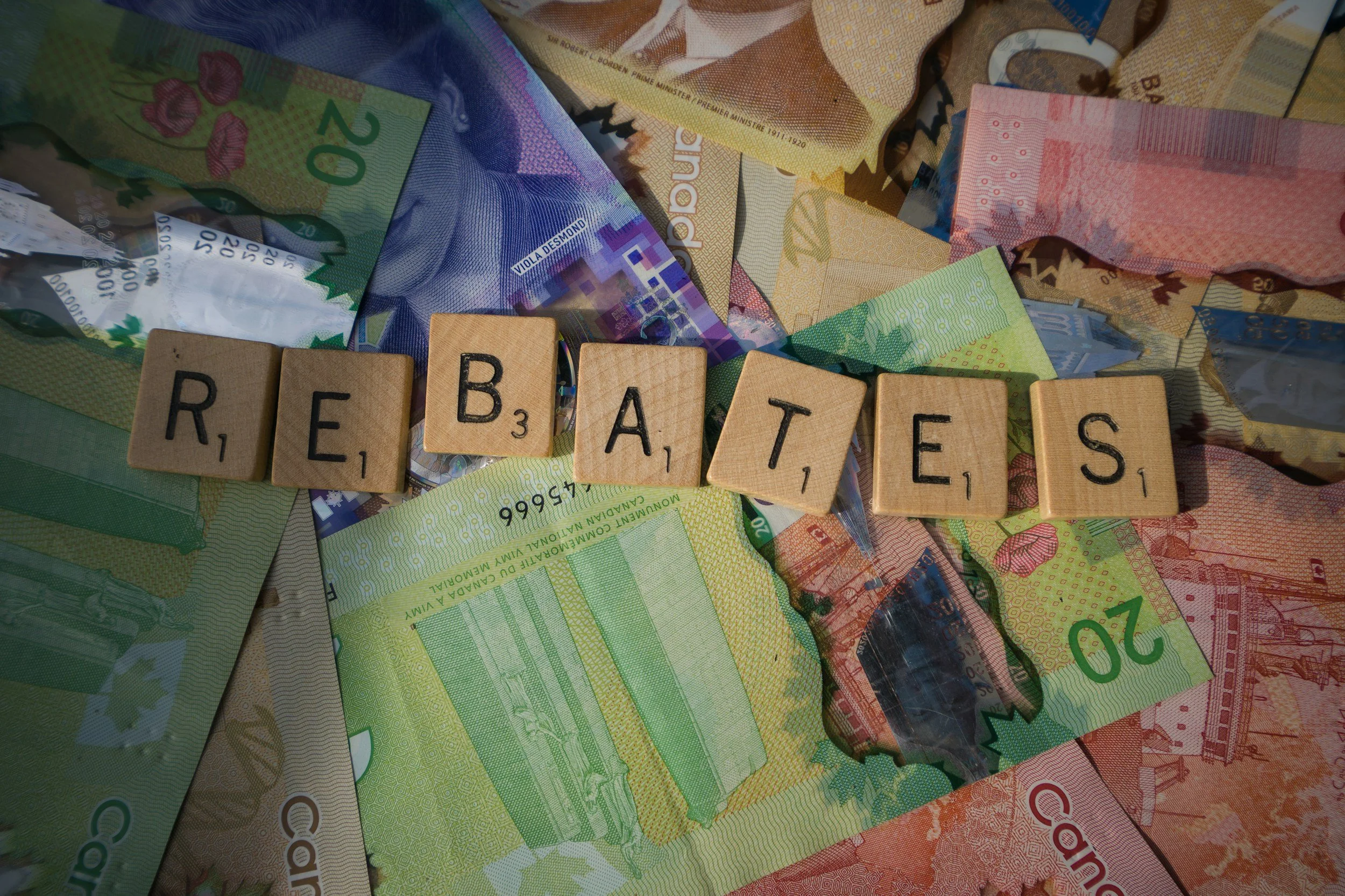 Scrabble tiles spelling 'REJECTES' placed on a scattered pile of various Canadian currency notes.