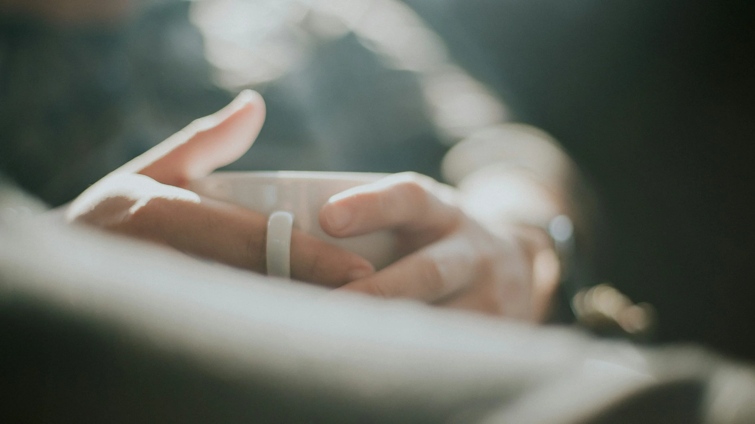 Close-up of a person's hand holding a white cup, with a blurred background of lights.