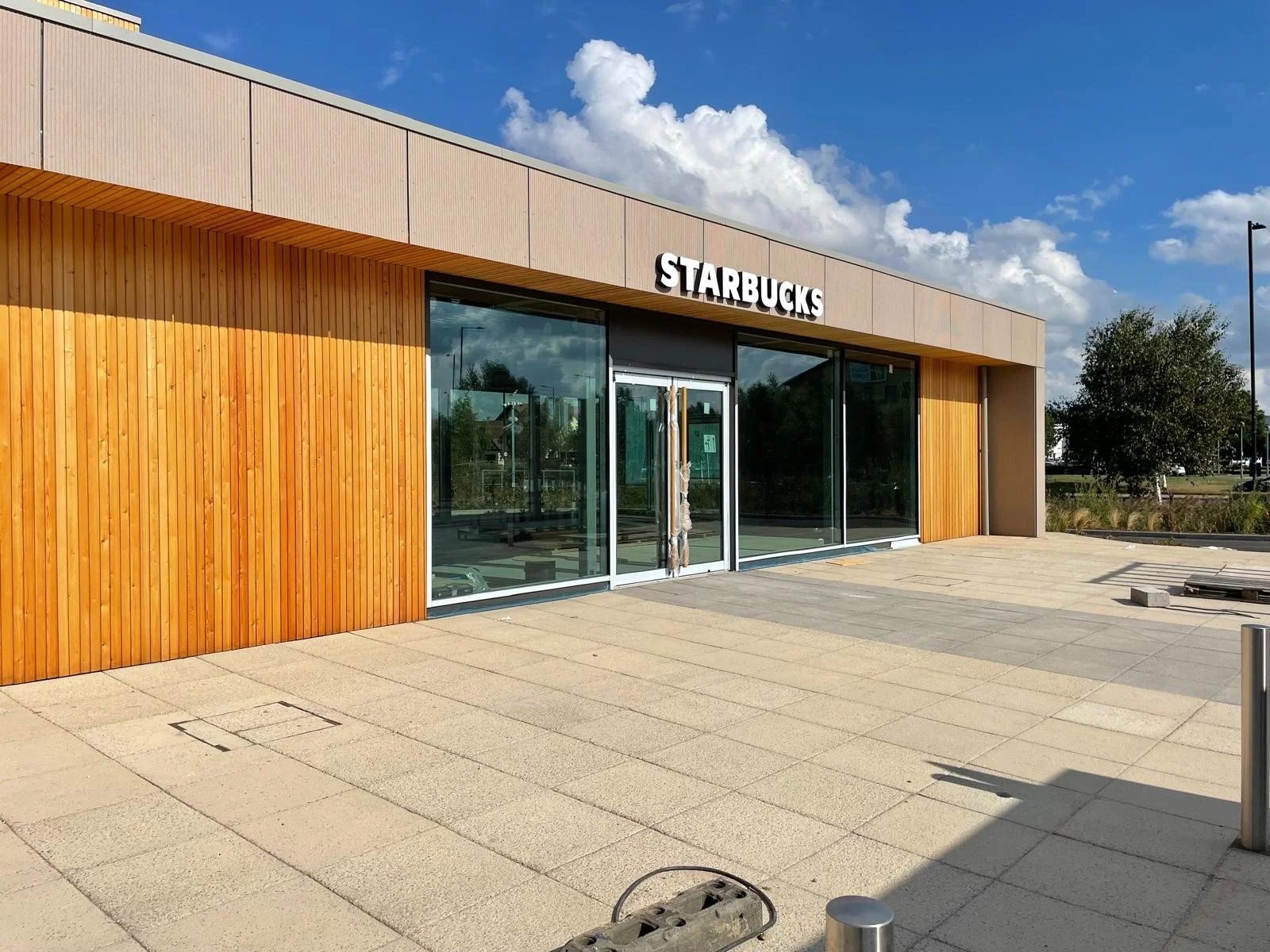 Front of a new Starbucks store with large glass windows and wooden exterior, under a partly cloudy sky.