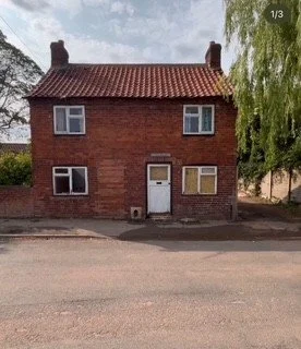 Two-story brick house with a red tiled roof and white-framed windows, situated on a suburban street with trees on each side.